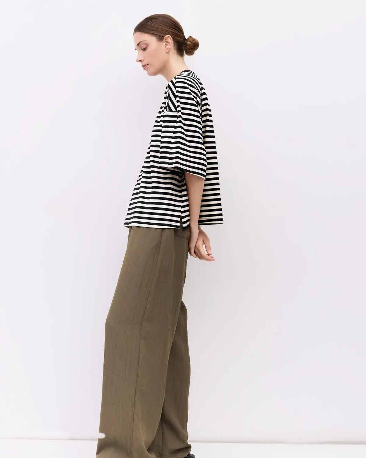 Woman wearing a black and white striped shirt and green pants against a white background