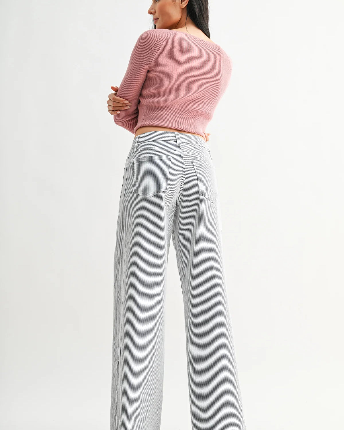 Woman wearing a pink sweater and gray checkered pants on a white background