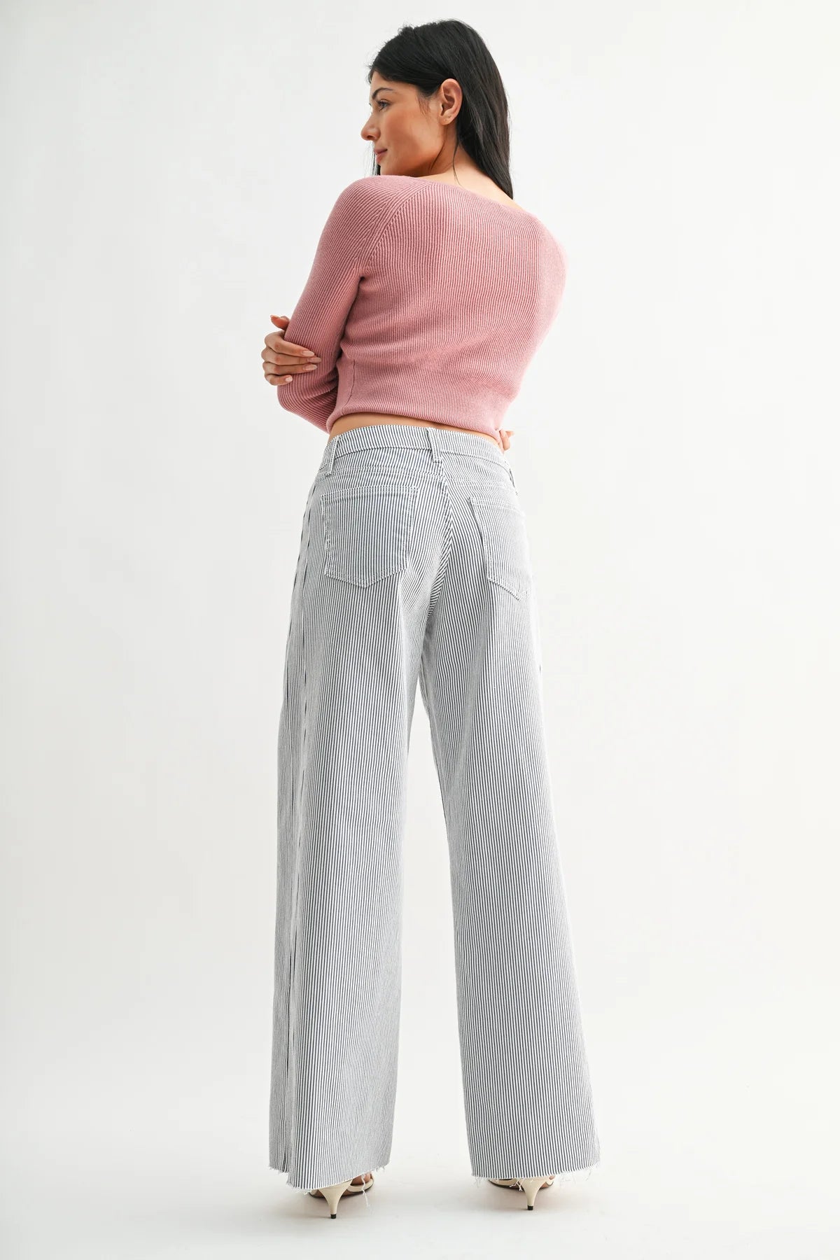 Woman wearing a pink sweater and gray checkered pants on a white background
