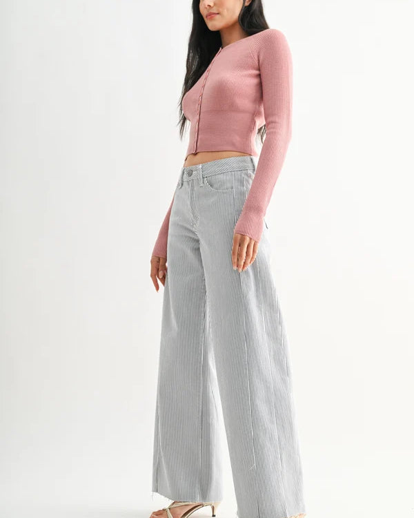 Woman wearing a pink cropped cardigan and light gray wide-leg jeans on a white background