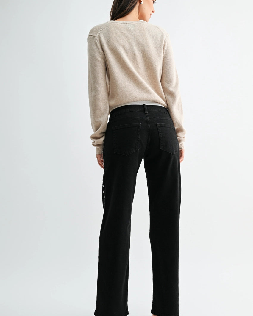 woman wearing black jeans and a cream sweater in front of a white background.