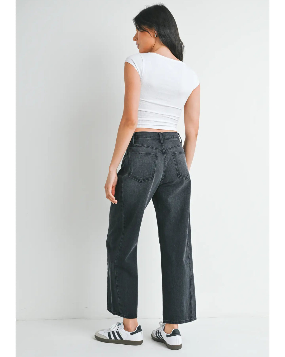 woman wearing black jeans and white top in front of a white background.