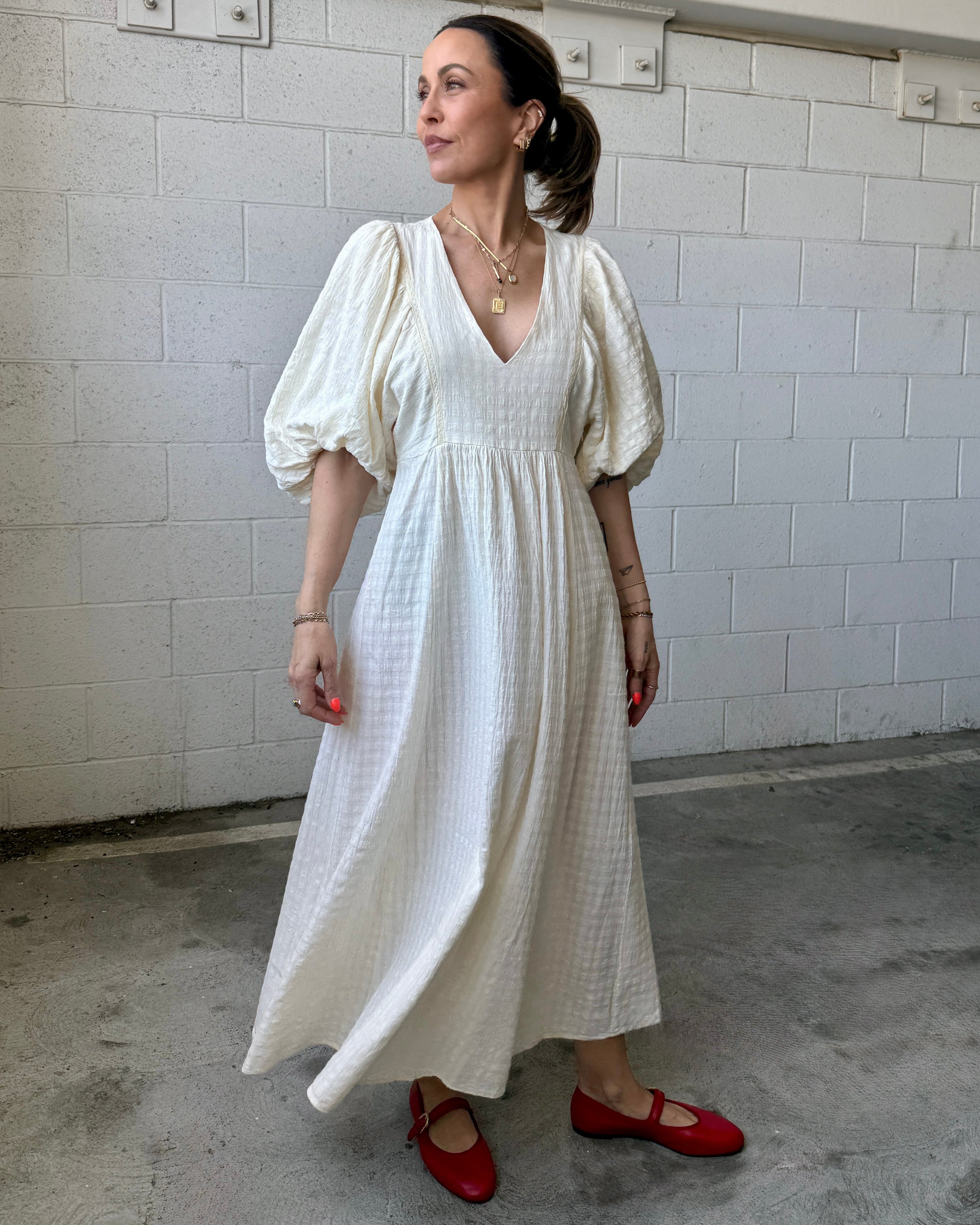 Woman in a white dress with puffed sleeves standing against a tiled wall.