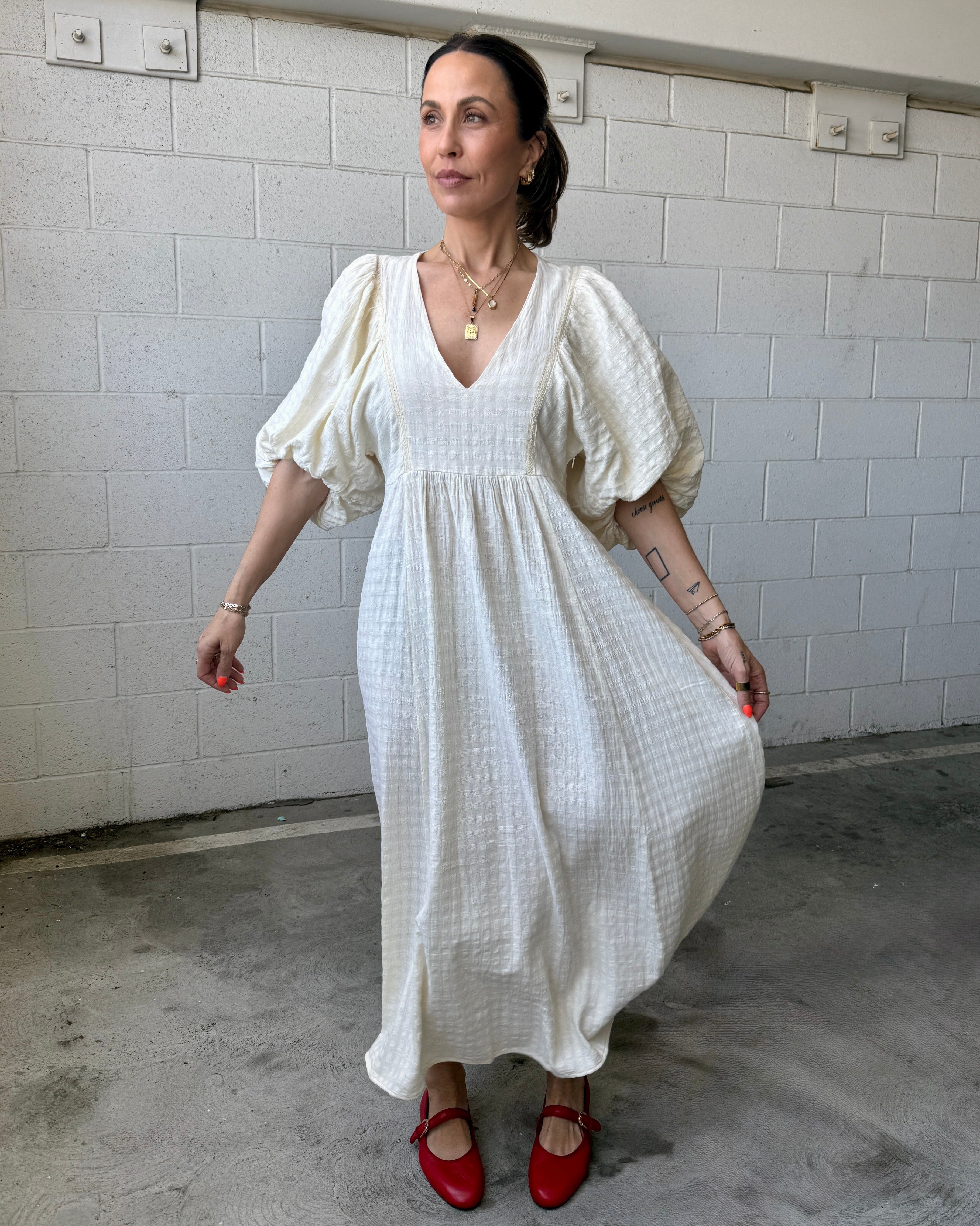 Woman wearing a white dress with puffed sleeves against a white tiled wall.