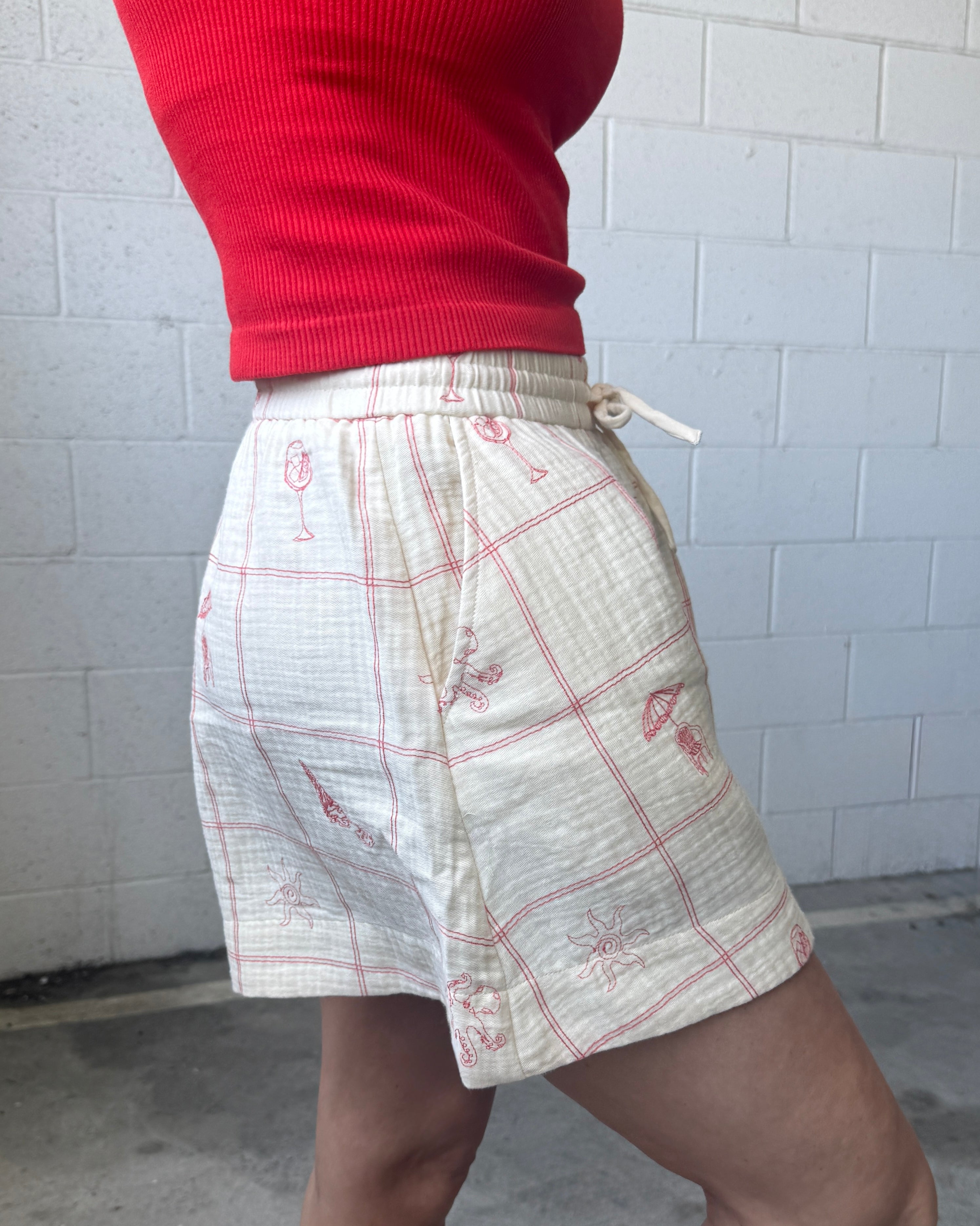 Person wearing a red top and white shorts with red patterns against a white tiled wall.