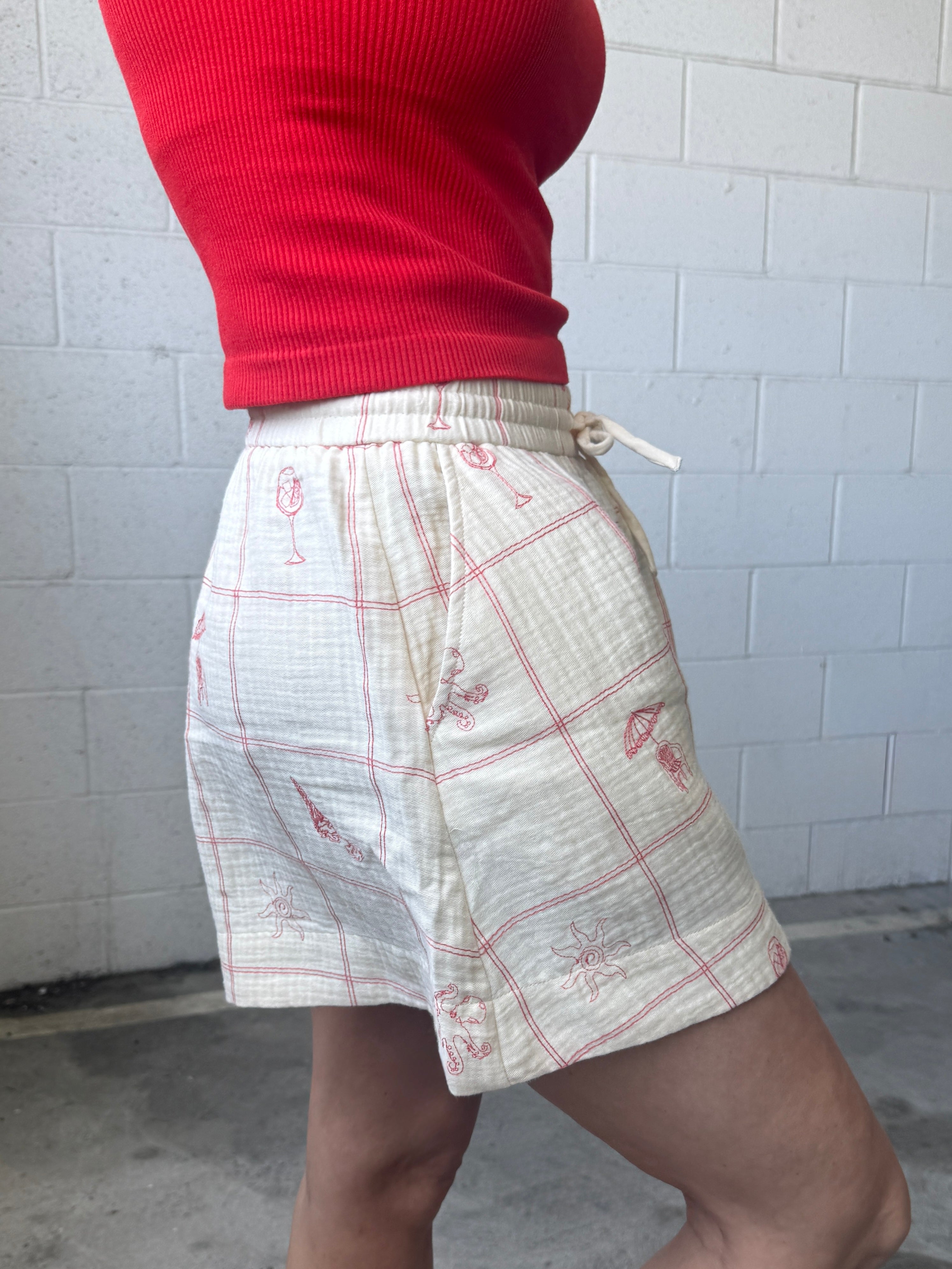 Person wearing a red top and white shorts with red patterns against a white tiled wall.