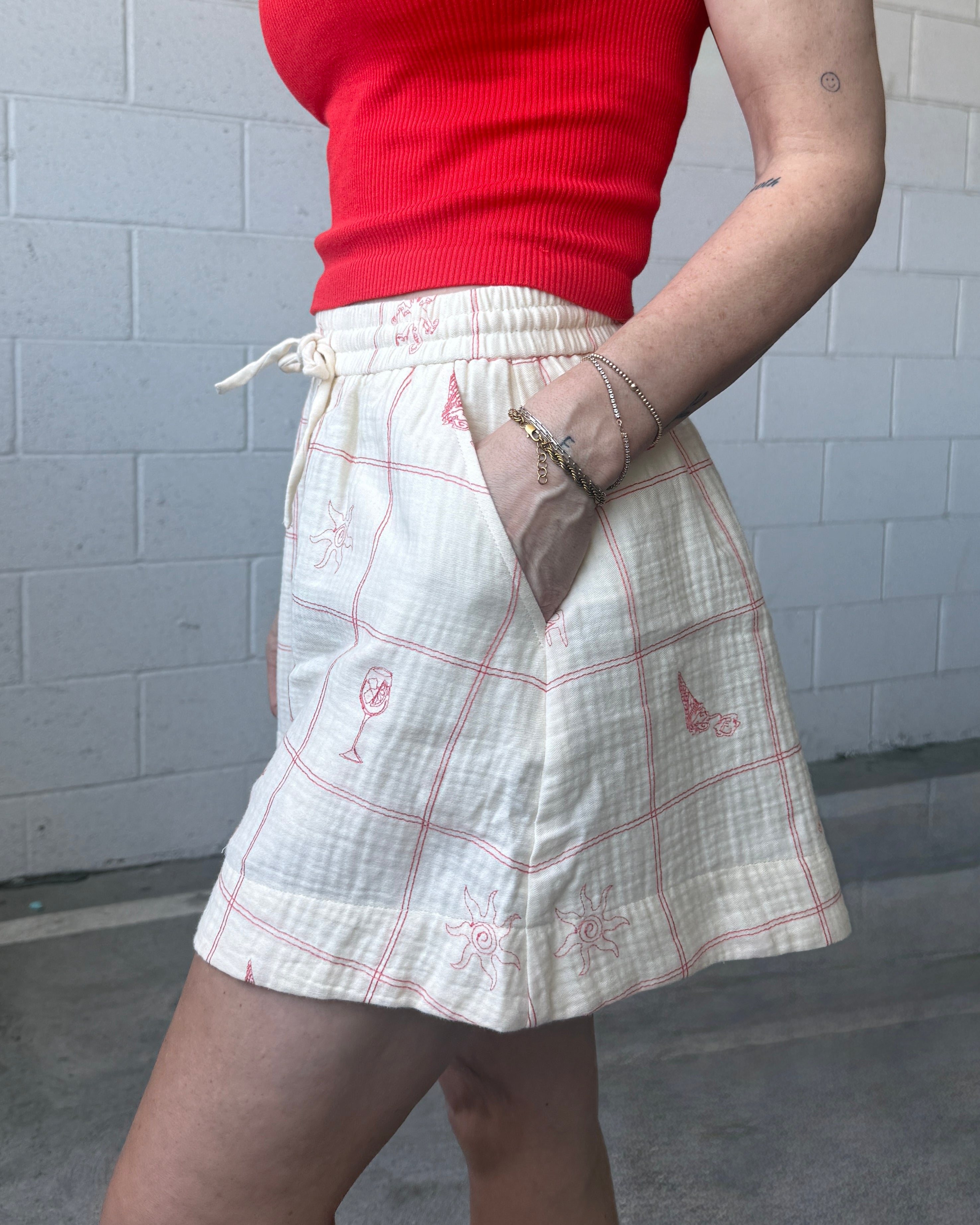 Person wearing a red top and white plaid skirt against a gray tiled wall.