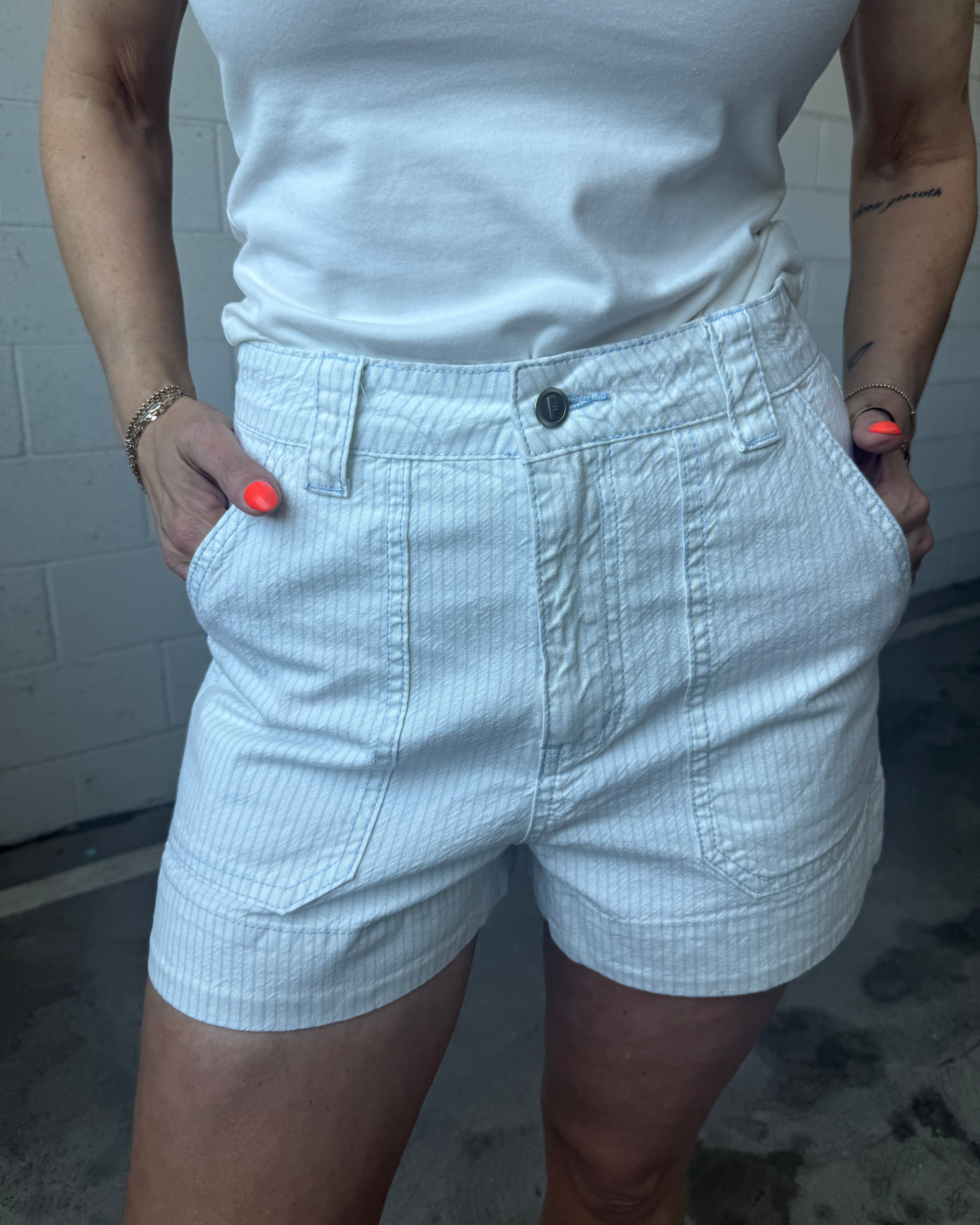 Person wearing light-colored shorts and a white top against a brick wall.