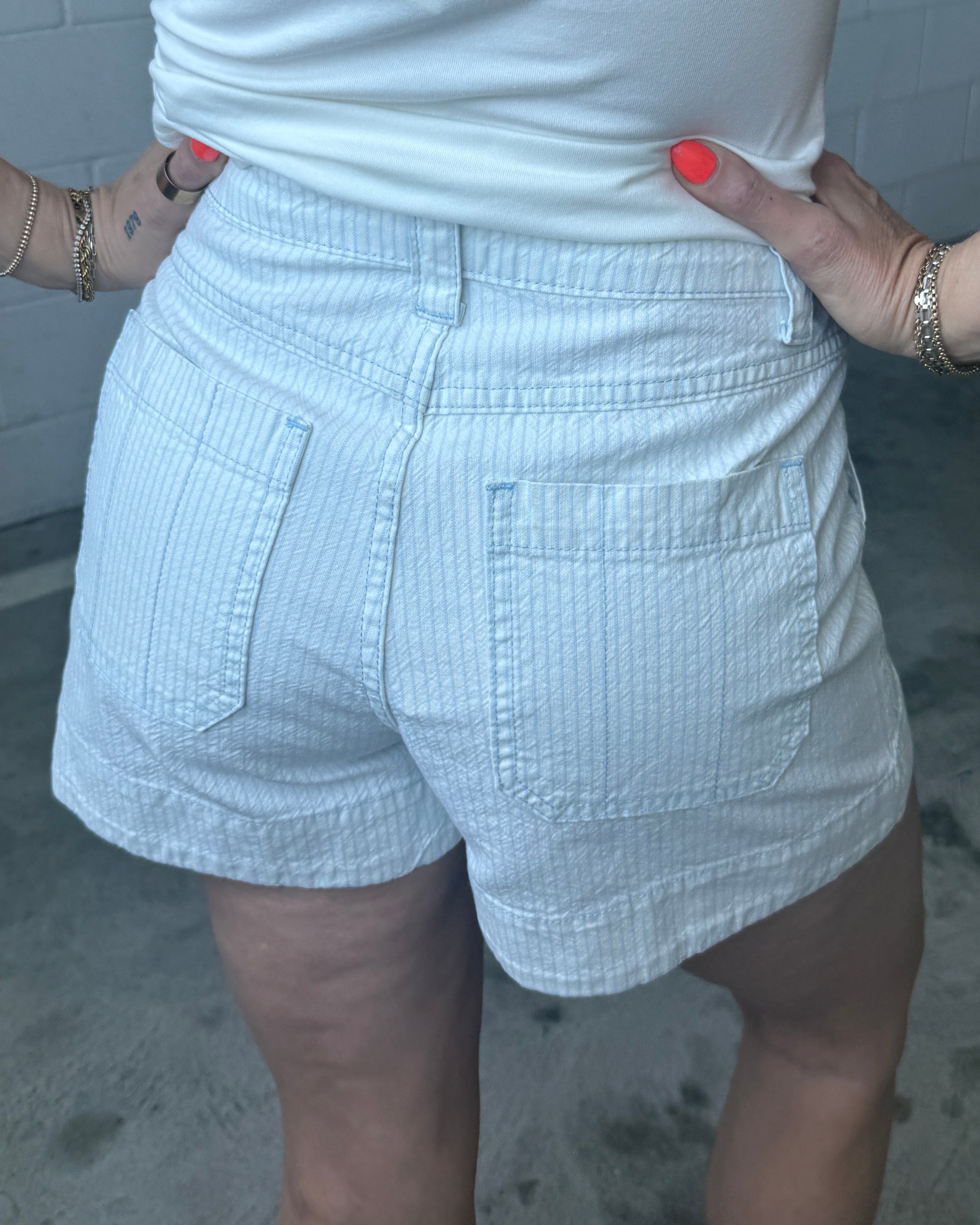Person wearing light blue shorts and a white top with a neutral background