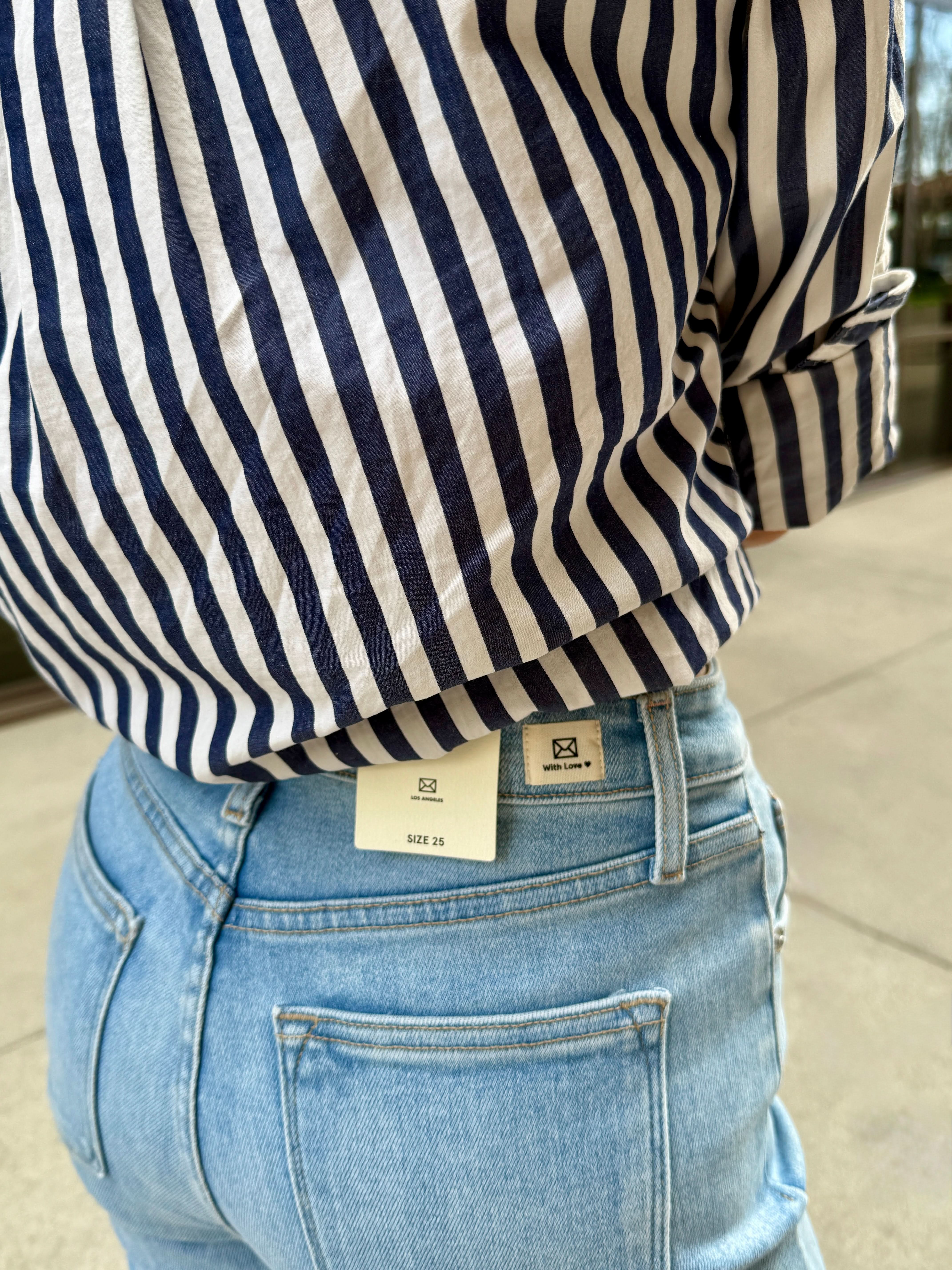 Woman standing outside wearing light wash raw hem jeans with black and white stripe blouse photo cropped to waistline