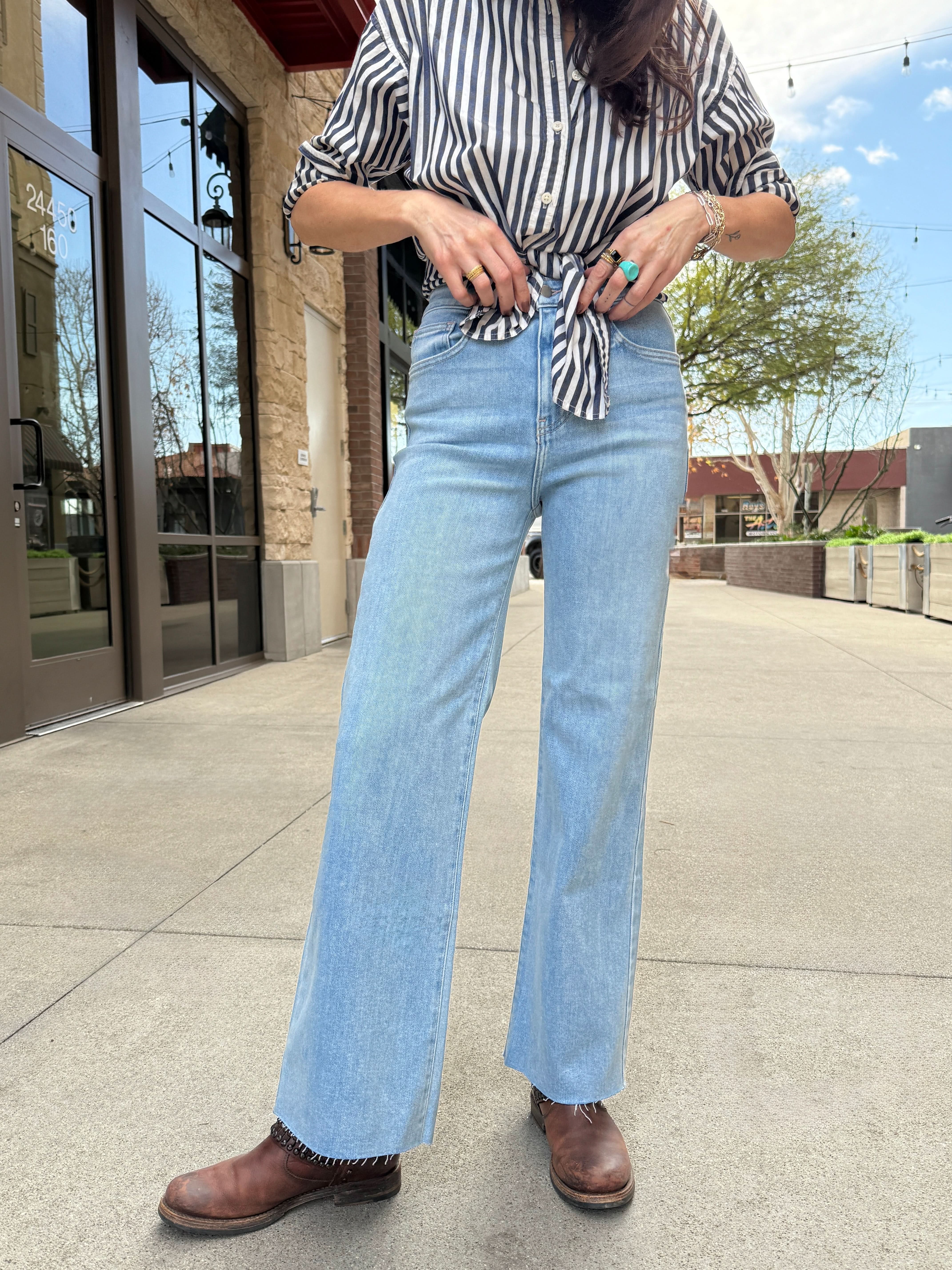 Woman standing outside wearing light wash raw hem jeans with black and white stripe blouse tied in front