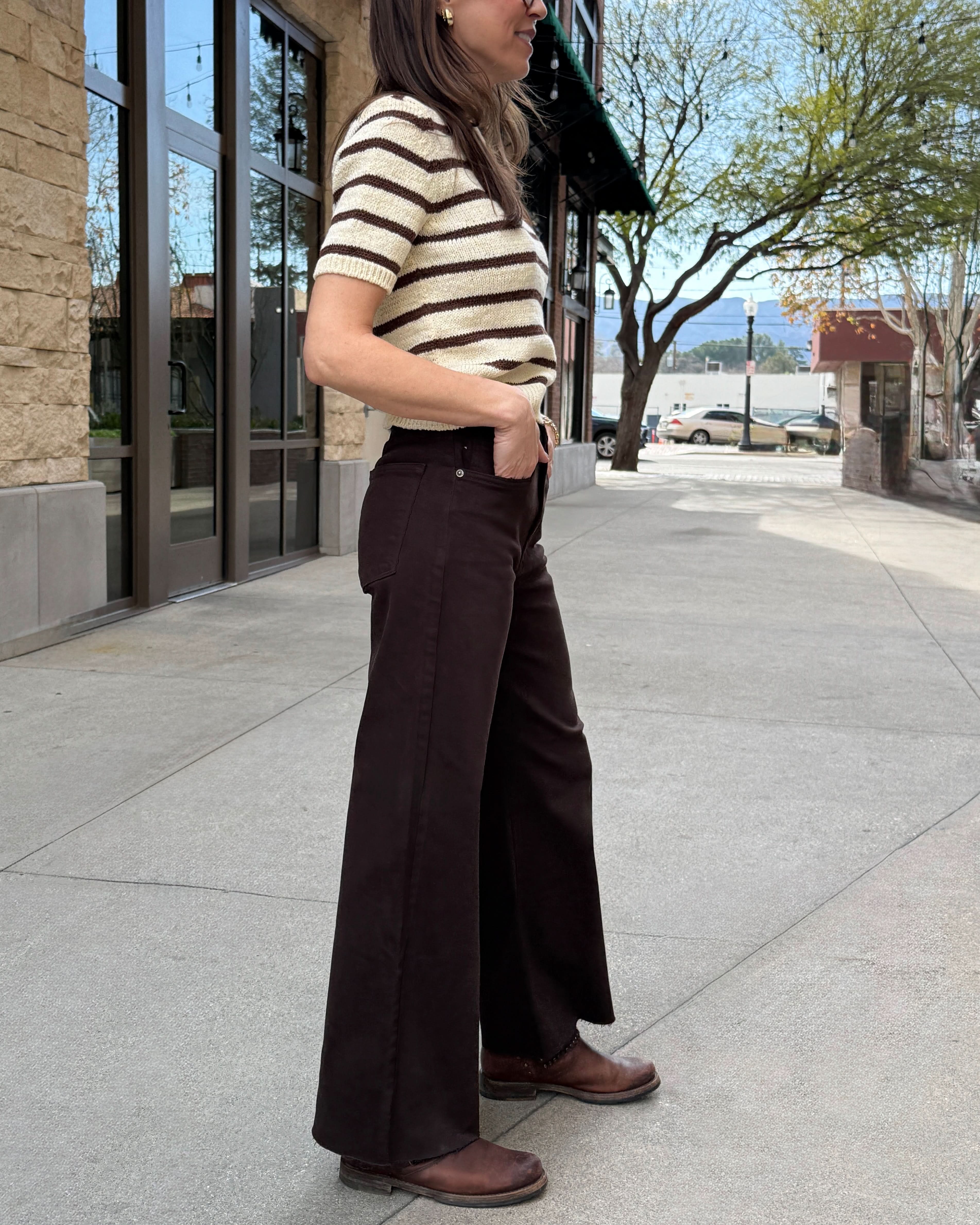Woman standing outside wearing brown raw hem jeans with stripe cream and brown stripped sweater.
