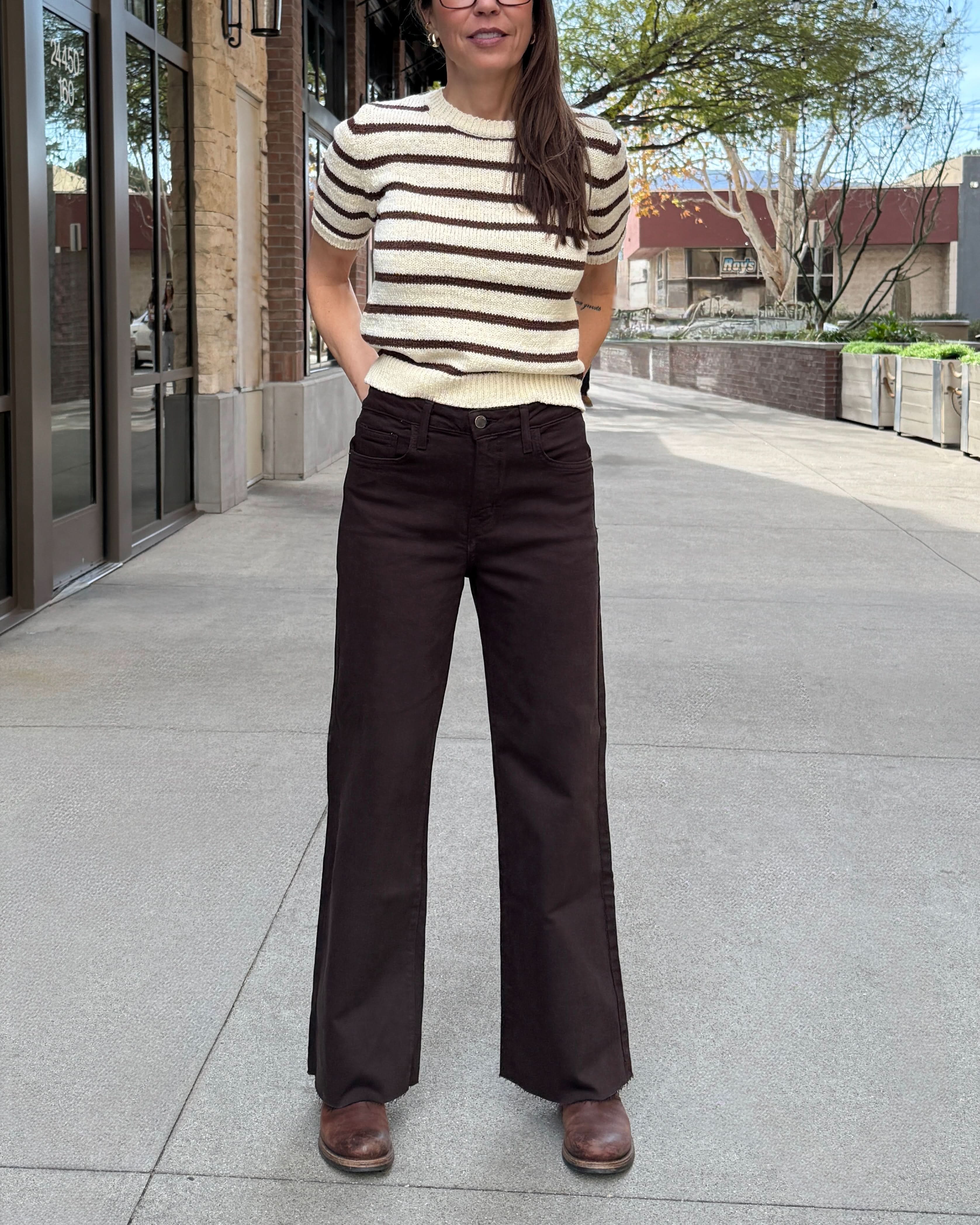 Woman standing outside wearing brown raw hem jeans with stripe cream and brown stripped sweater.