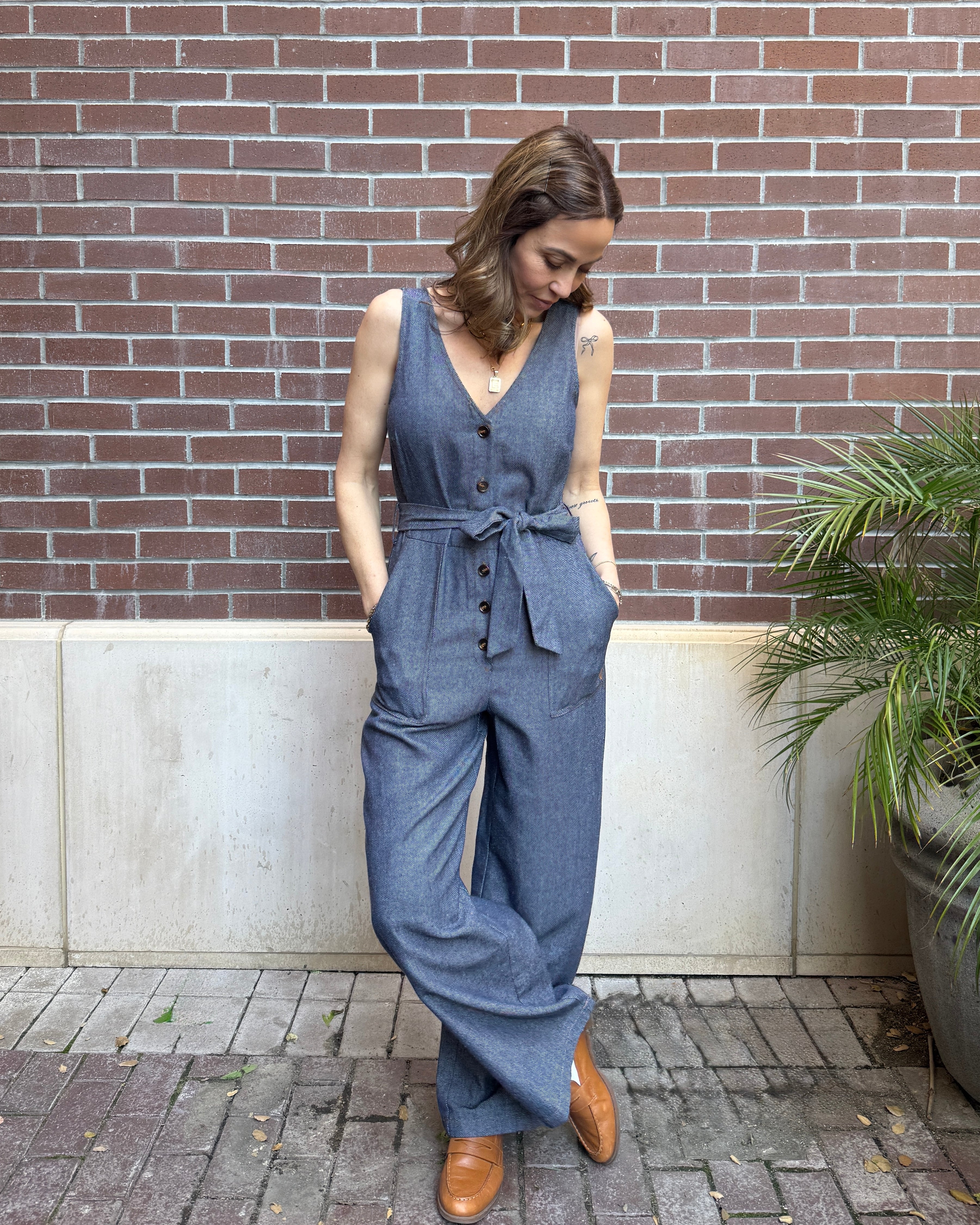 Woman wearing a blue jumpsuit standing against a brick wall.