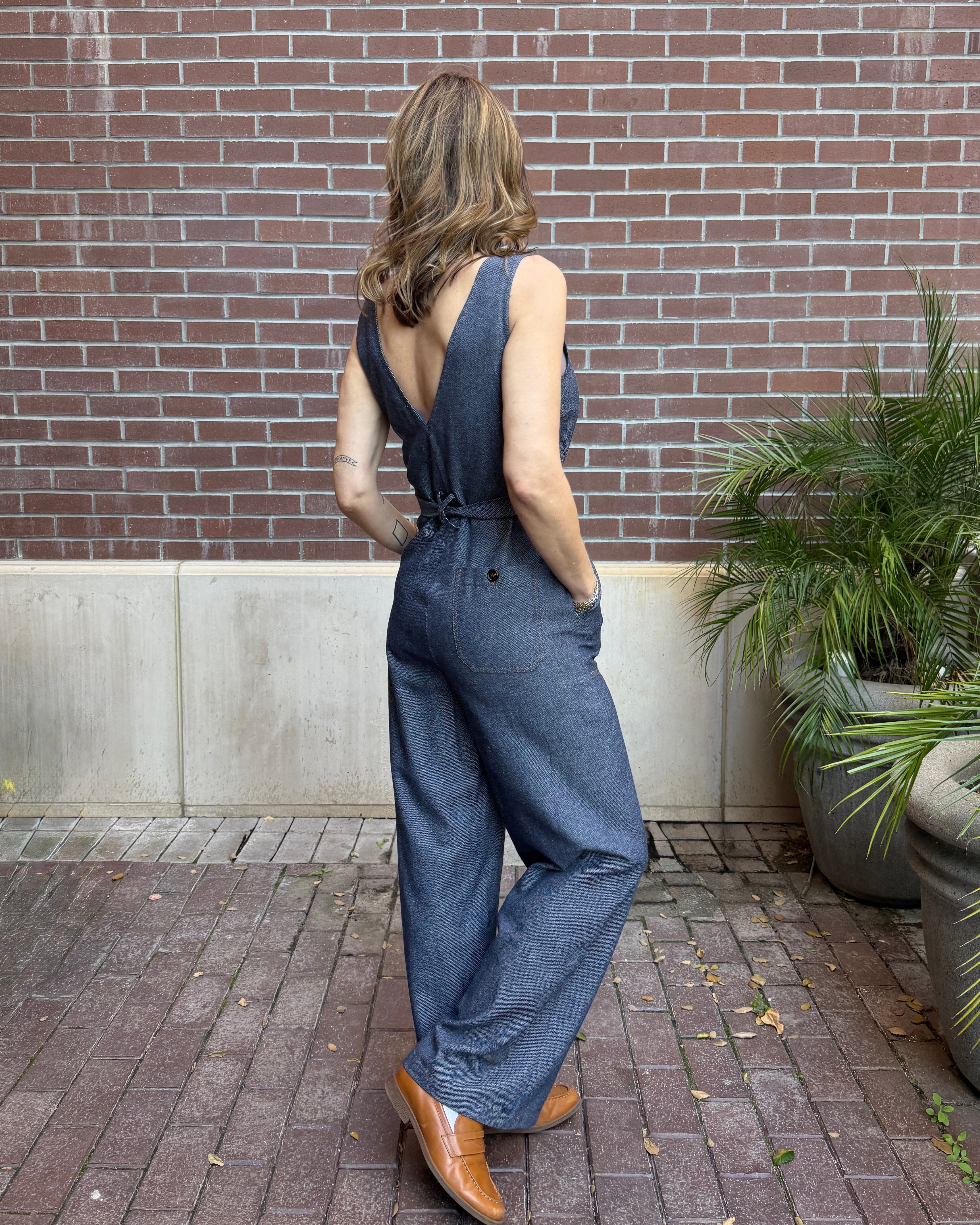 Woman wearing a blue denim jumpsuit standing in front of a brick wall.