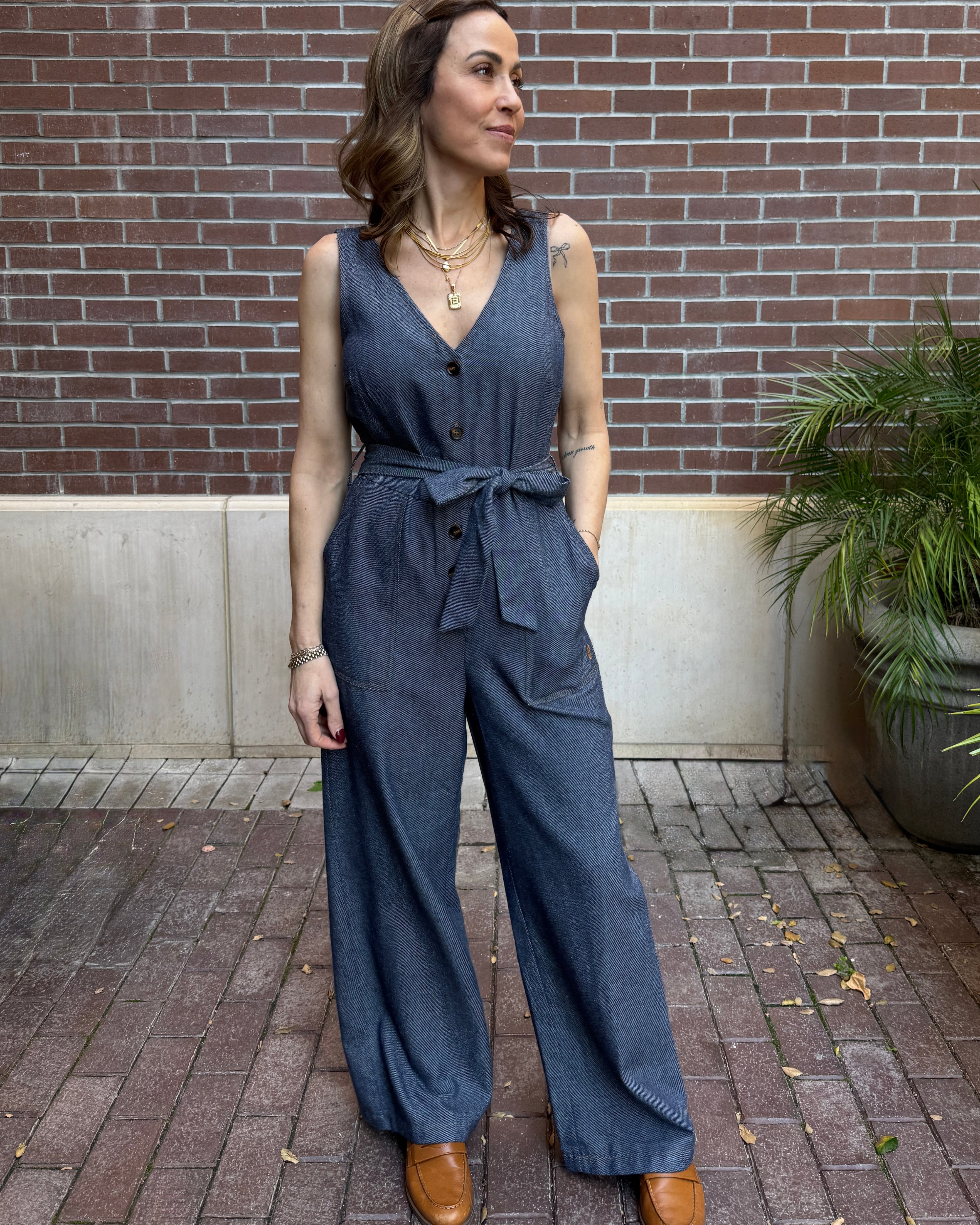 Woman wearing a blue jumpsuit standing against a brick wall.