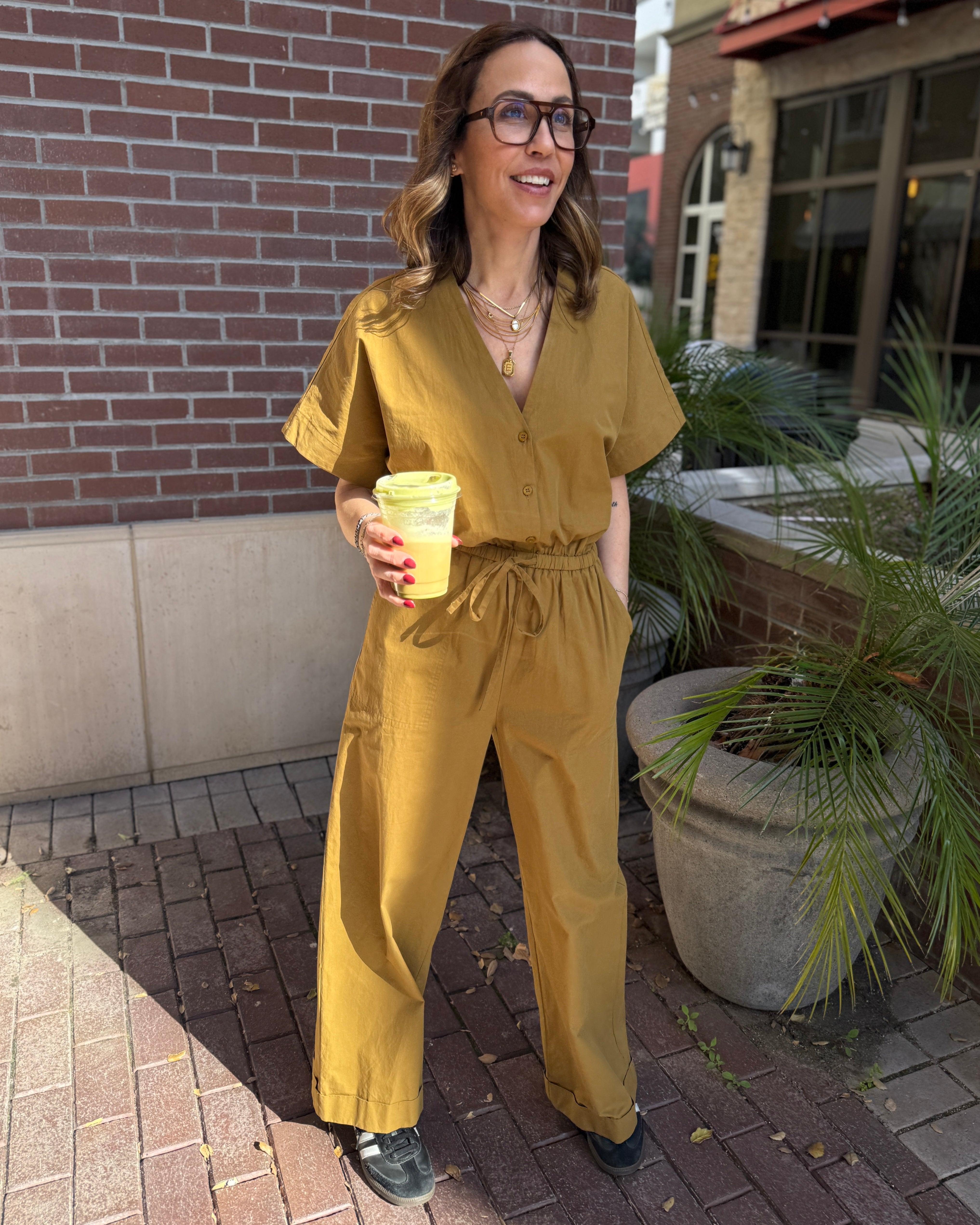 Person wearing a mustard yellow jumpsuit standing outdoors near a building.