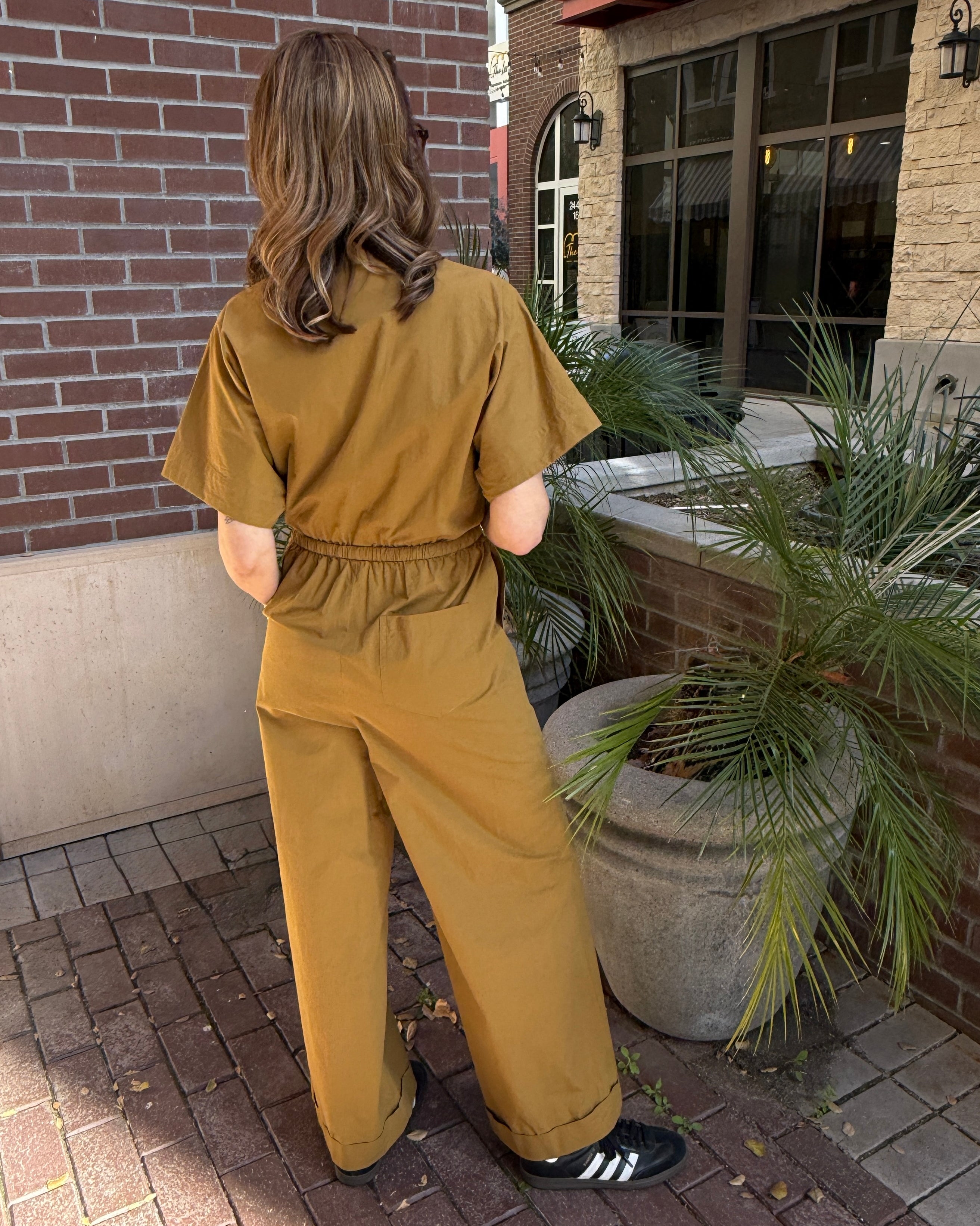 Person wearing a mustard yellow jumpsuit standing outdoors near a building.