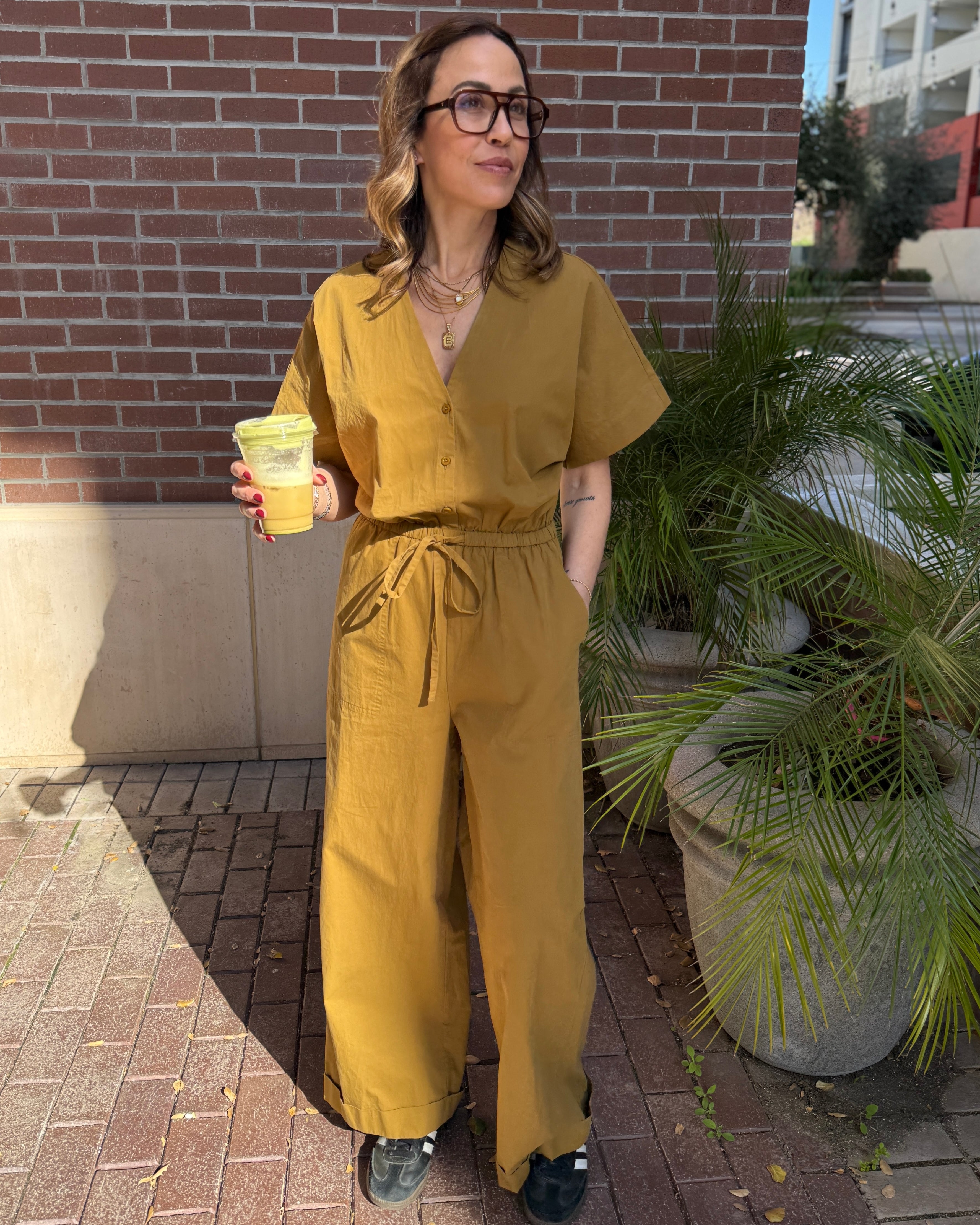 Person wearing a mustard yellow jumpsuit standing outdoors near a building.