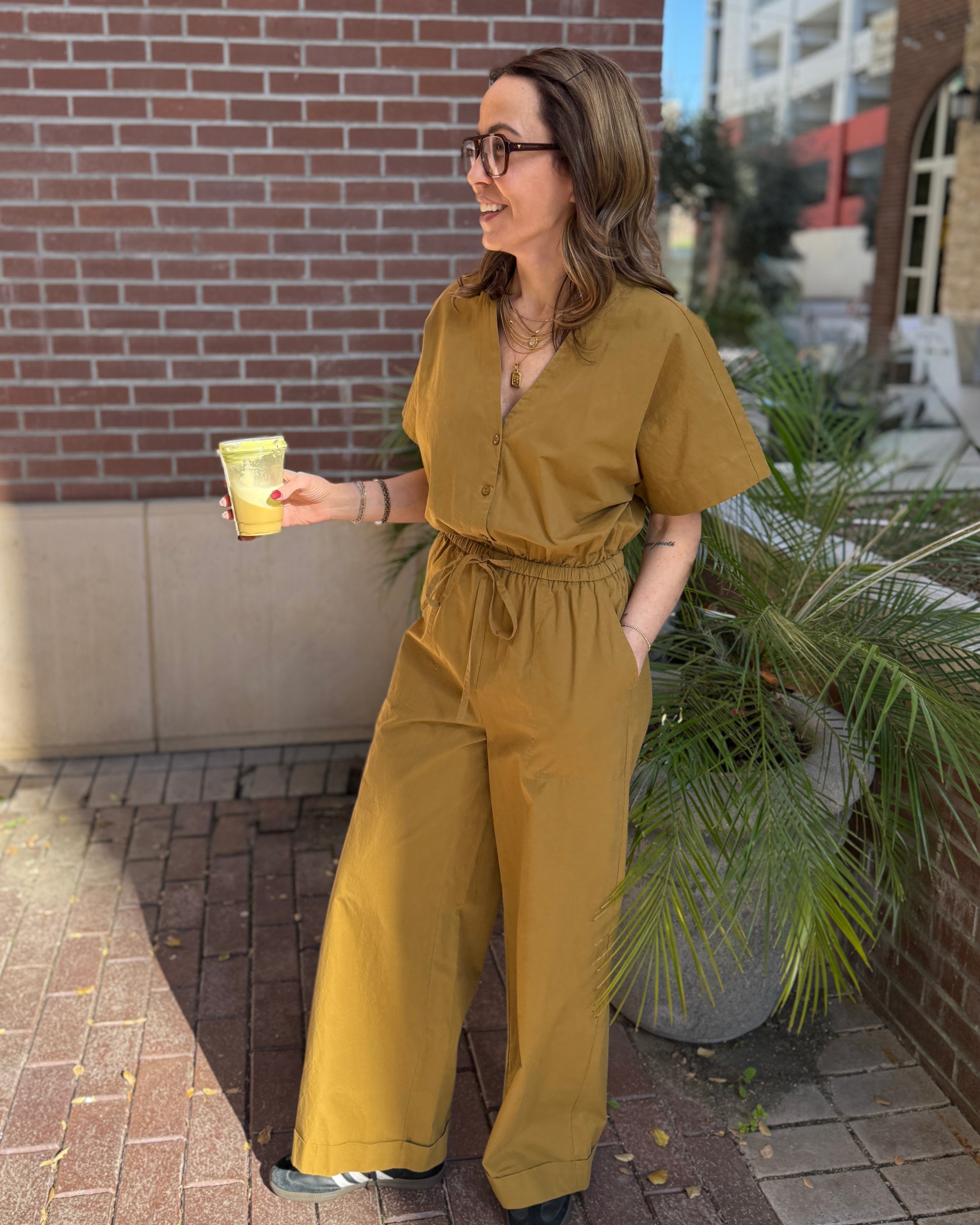 Person wearing a mustard yellow jumpsuit standing outdoors near a building.