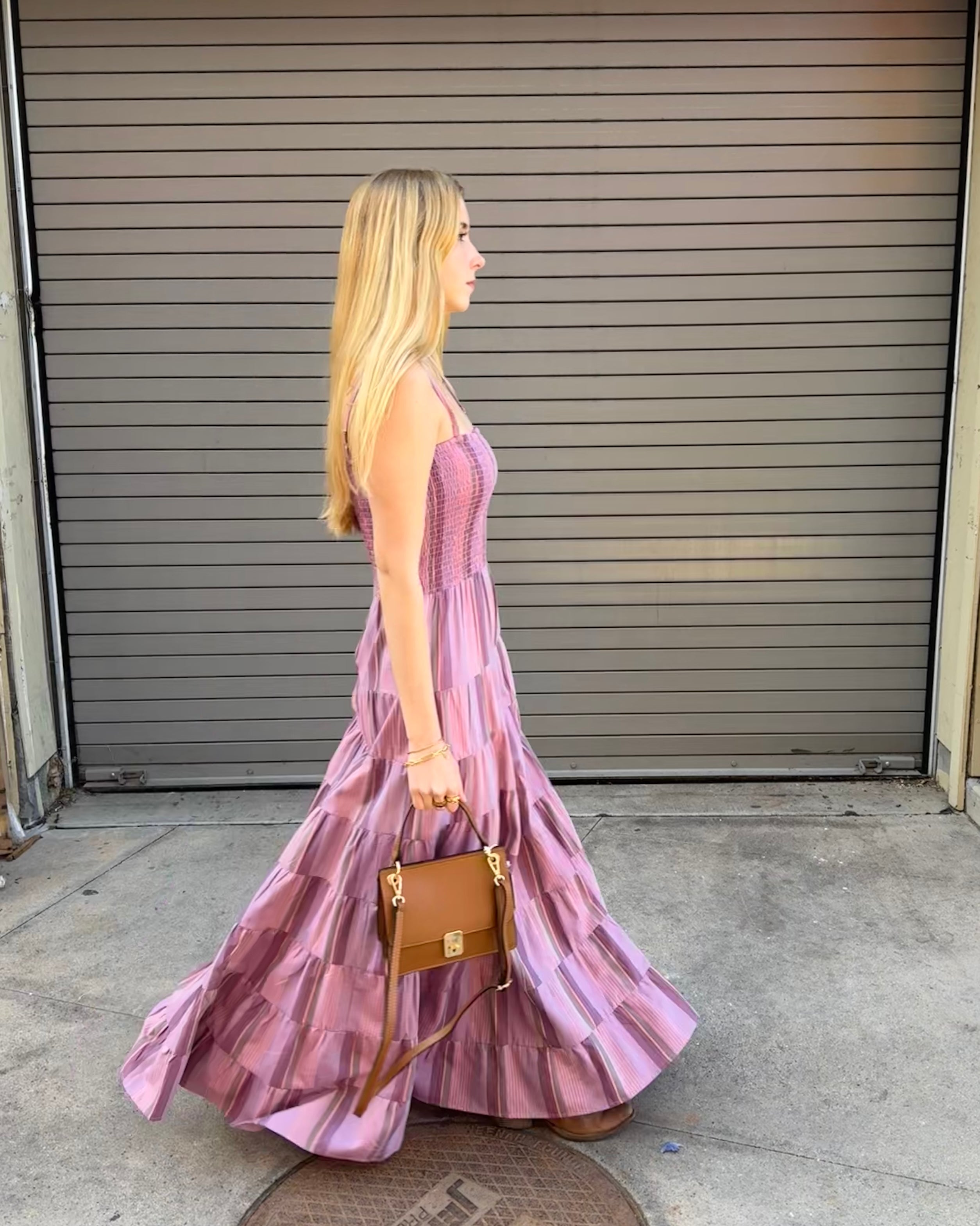 Woman in a pink dress holding a brown handbag in front of a closed garage door.