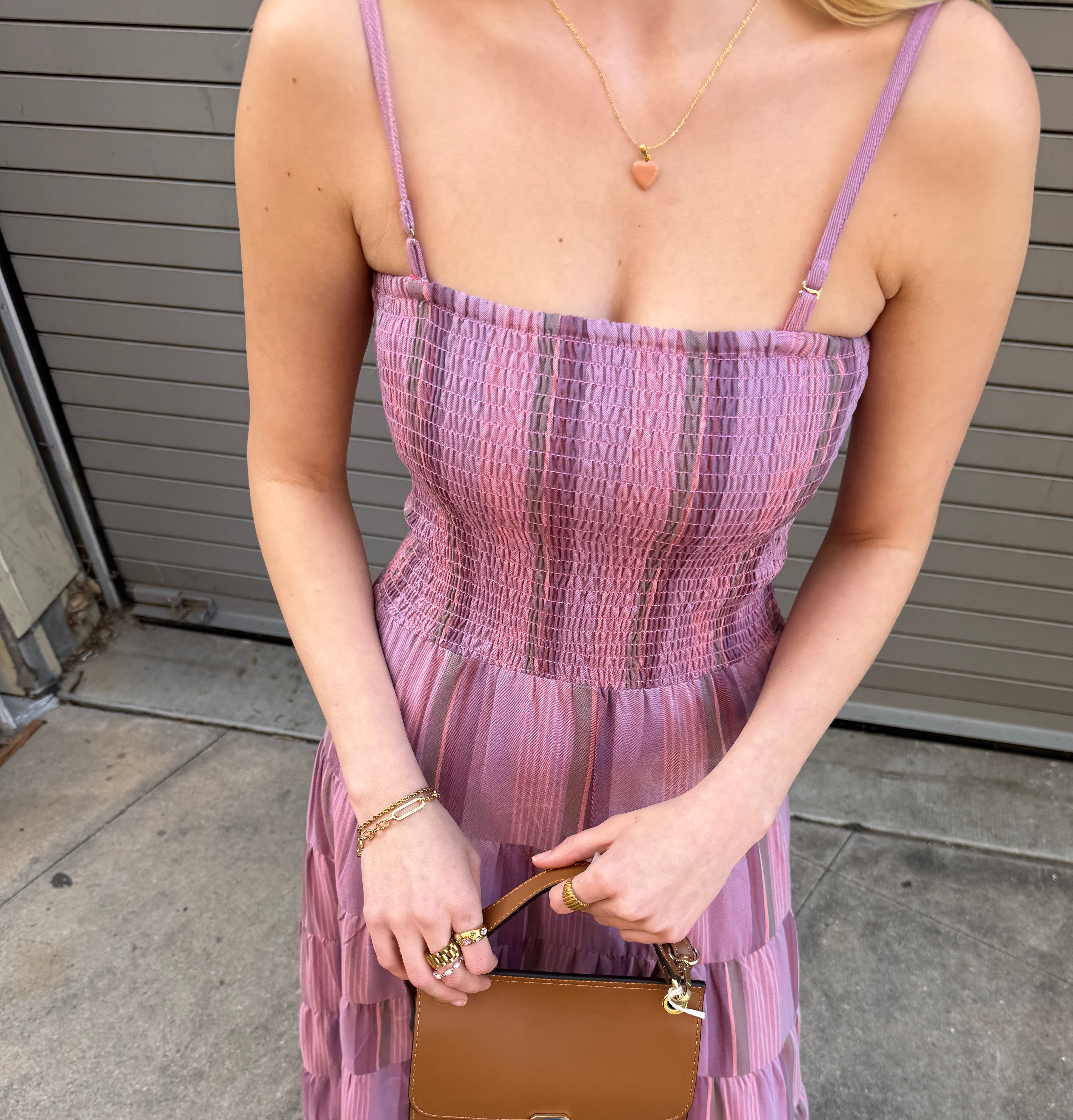 Woman in a pink dress holding a brown handbag on a concrete floor.