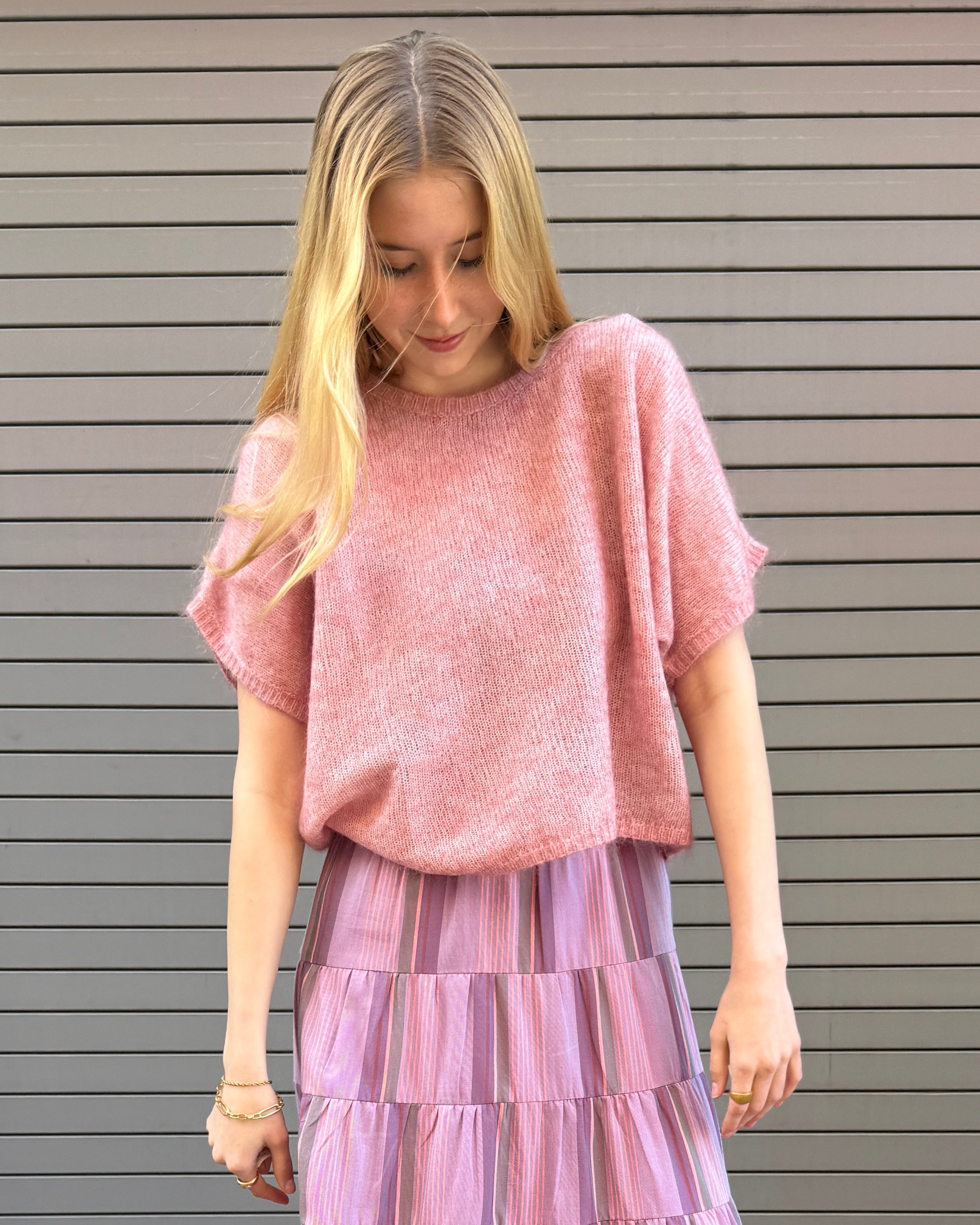 Woman wearing a pink top and purple skirt against a gray background