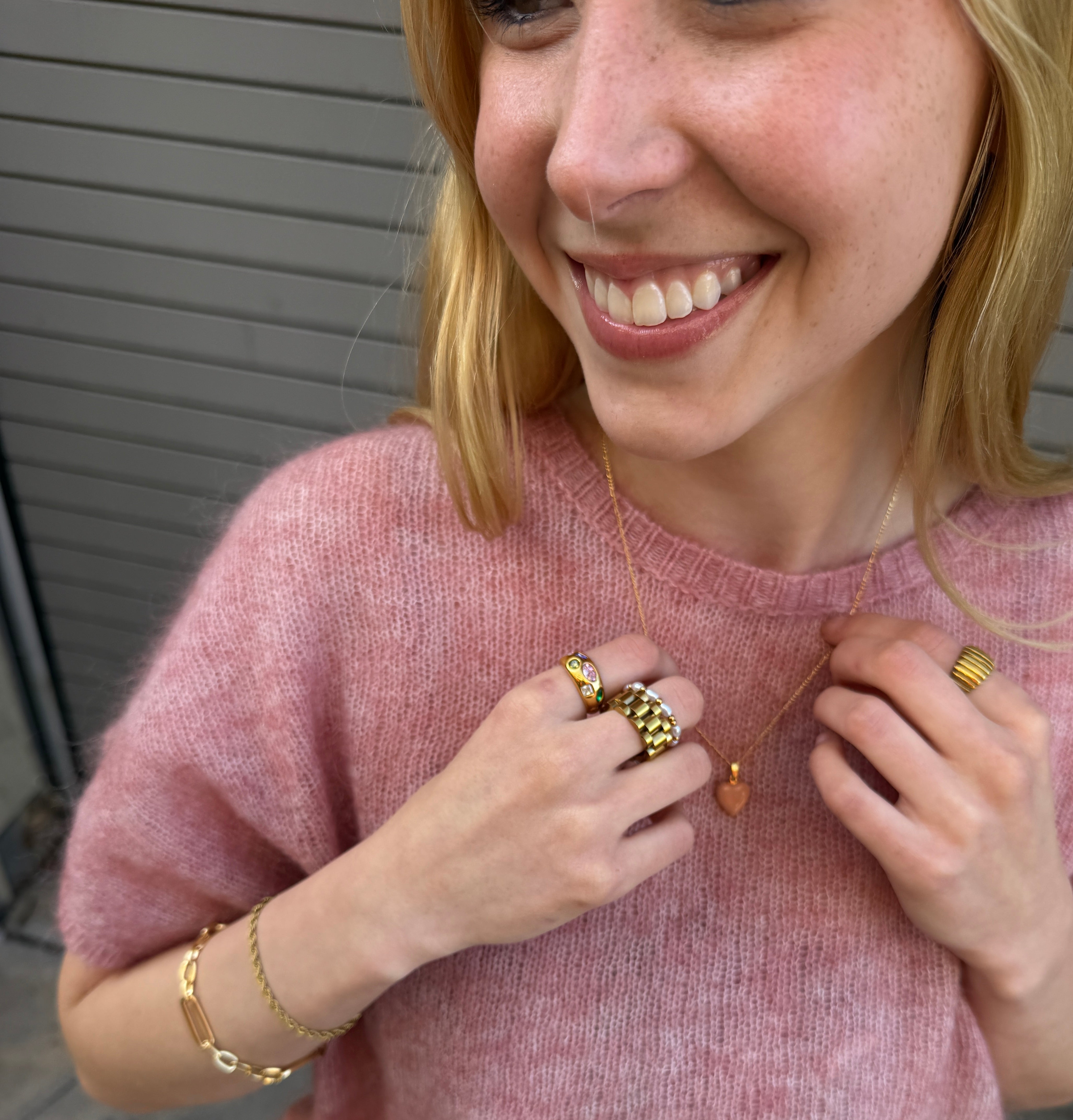 Woman wearing multiple rings and a bracelet on a pink sweater.