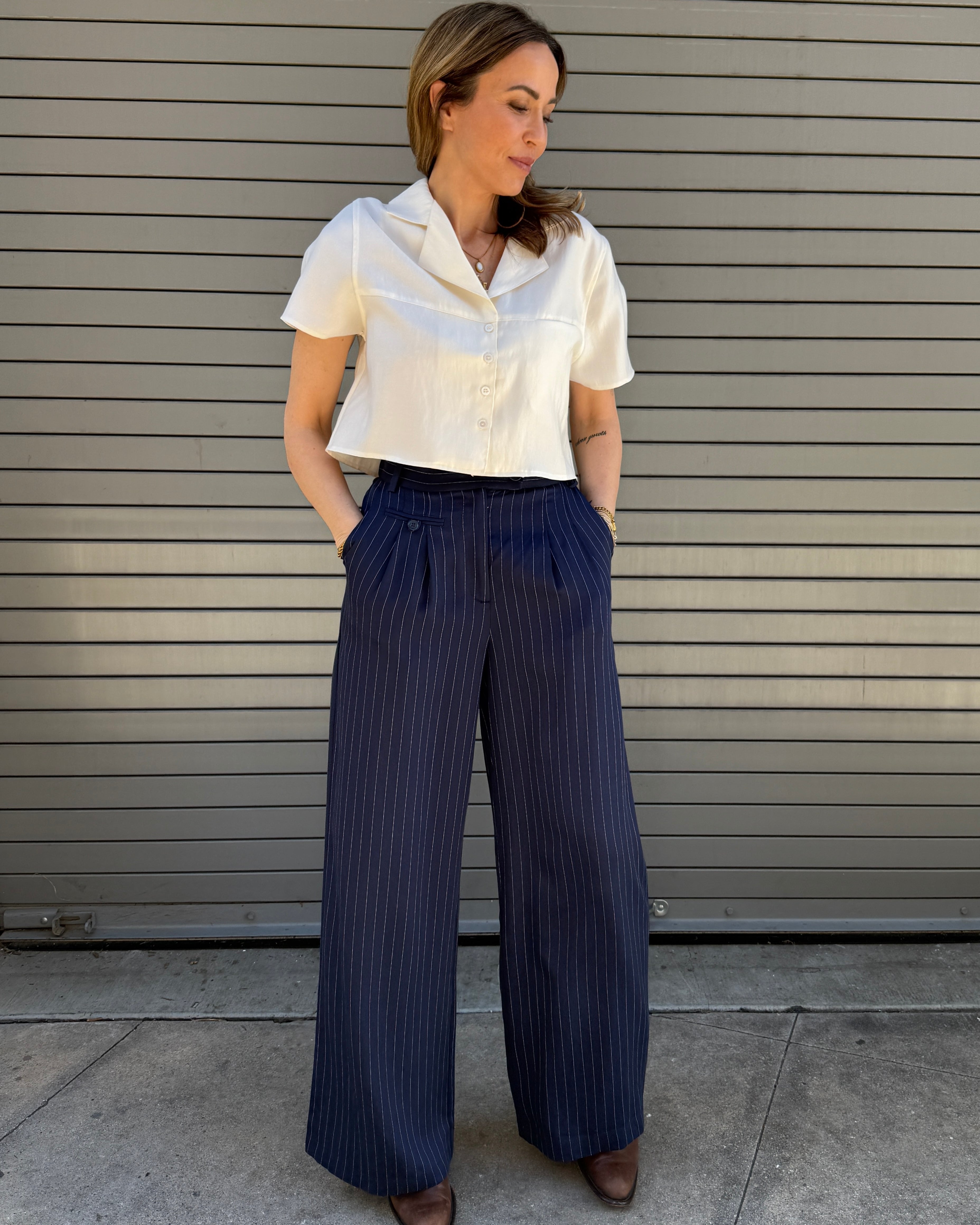 Woman wearing a white blouse and navy pinstripe pants standing against a gray wall.
