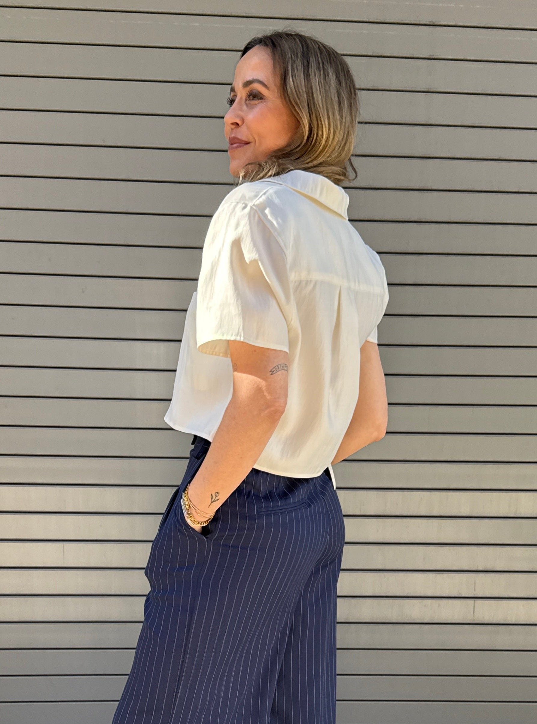 Woman wearing a white blouse and blue striped pants standing against a gray wall.