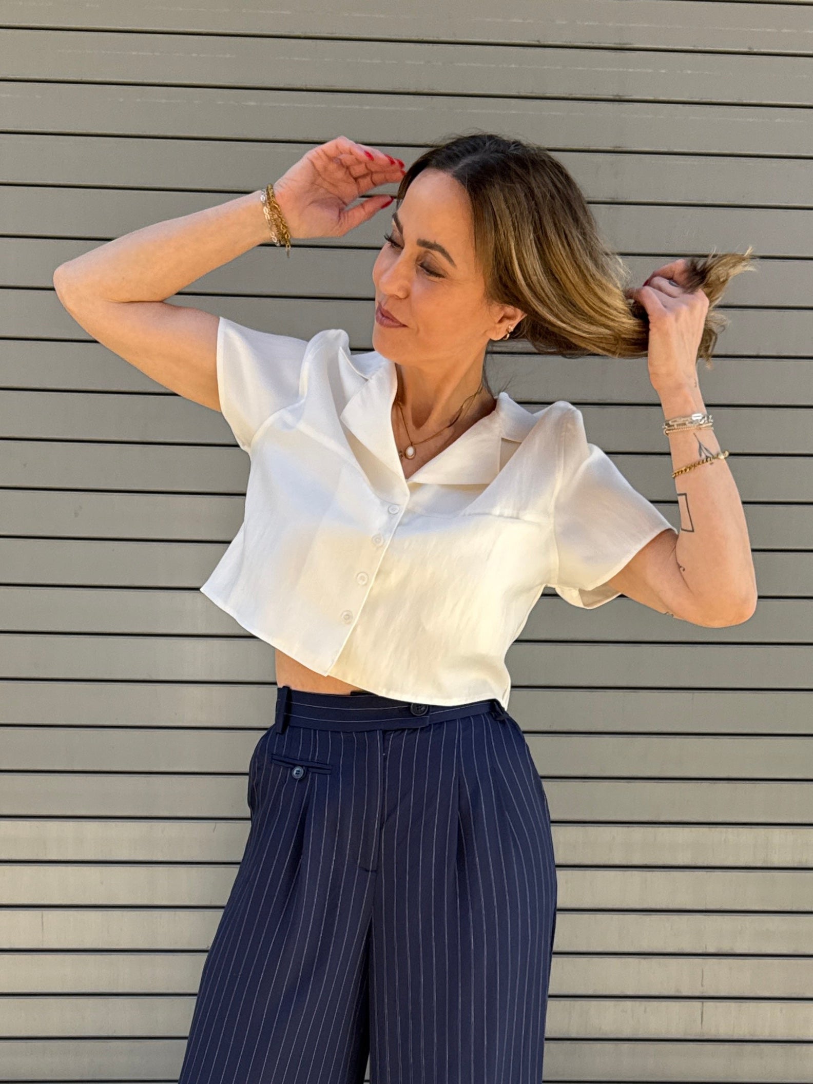 Woman wearing a white top and navy pinstripe pants against a gray background