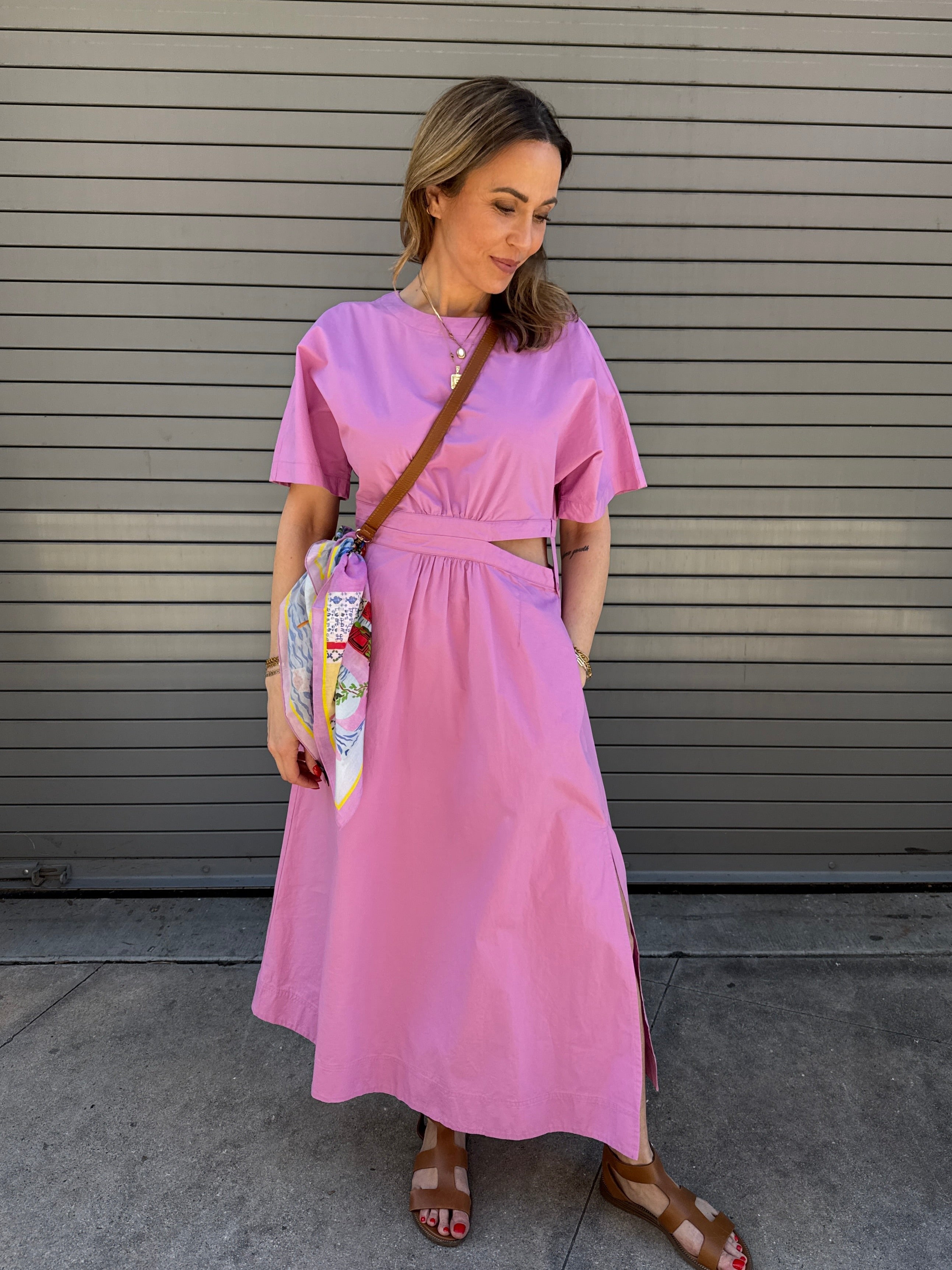 Woman wearing a pink dress standing in front of a gray metal shutter.