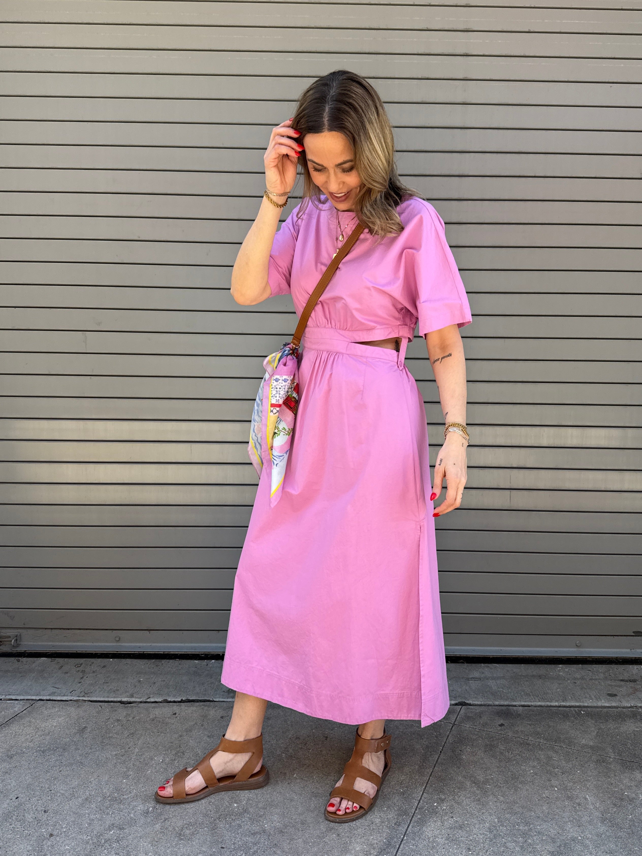 Woman wearing a pink dress standing in front of a gray shutter.
