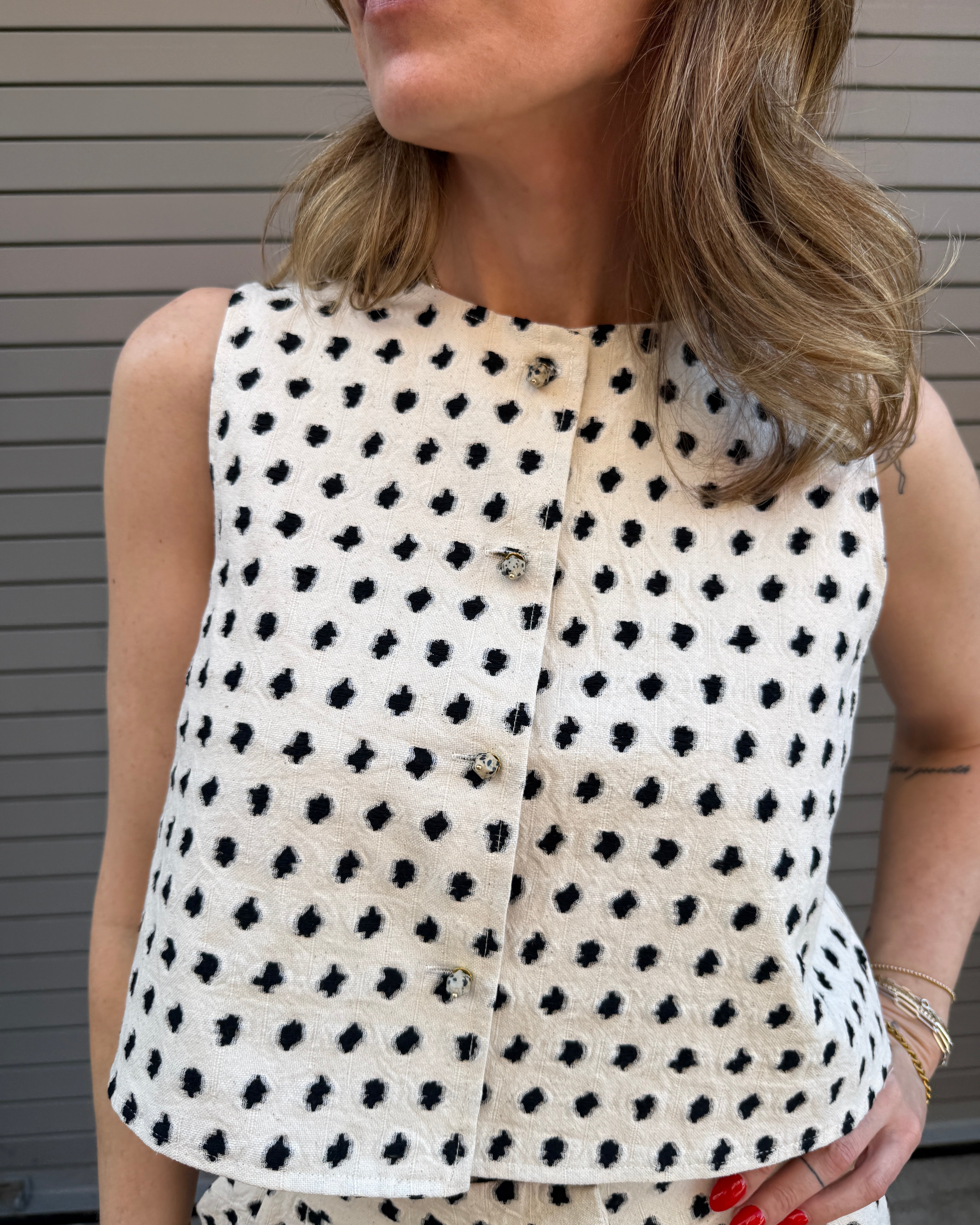 Woman wearing a white sleeveless top with black polka dot pattern.