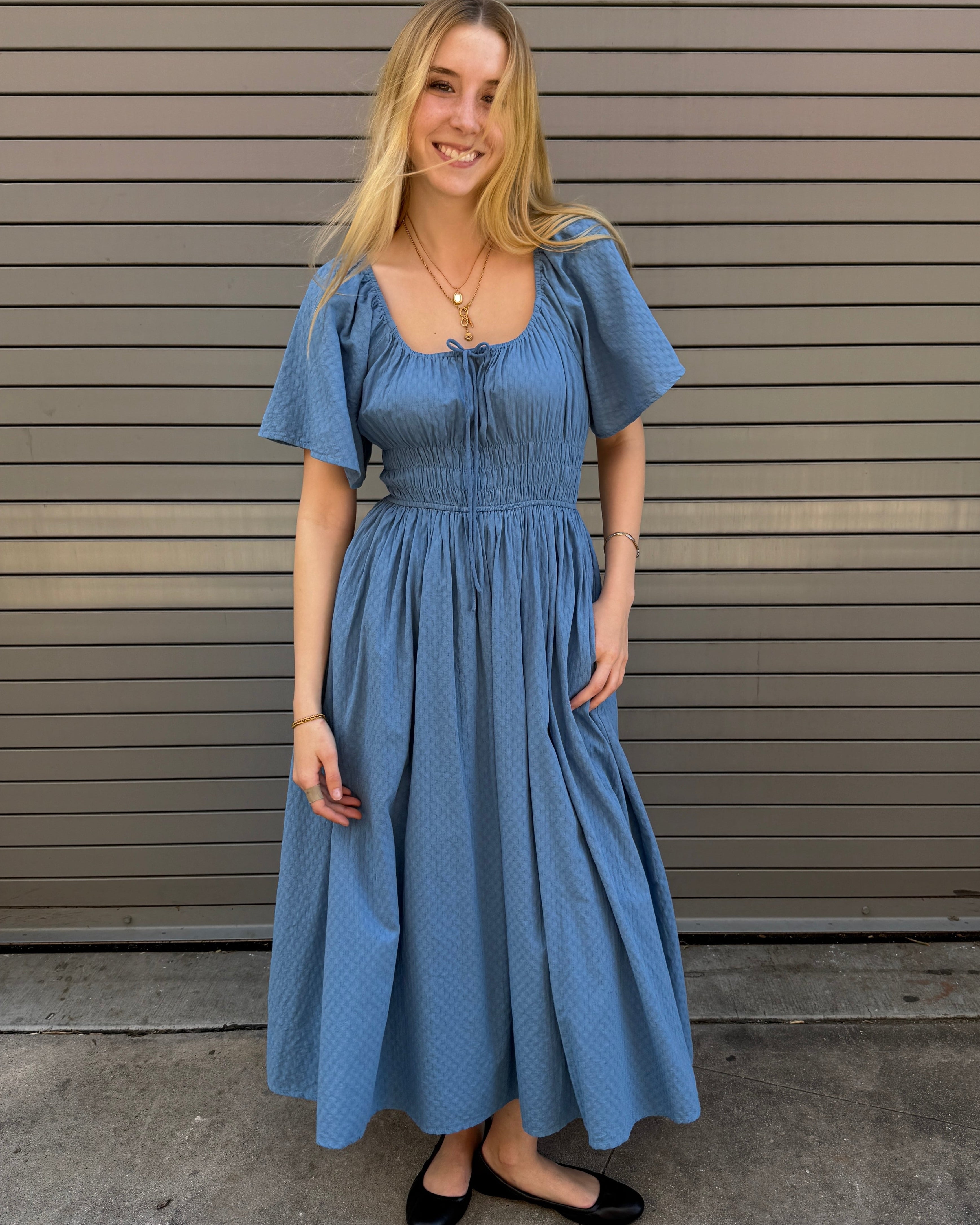 Woman wearing a blue dress standing in front of a metallic wall.