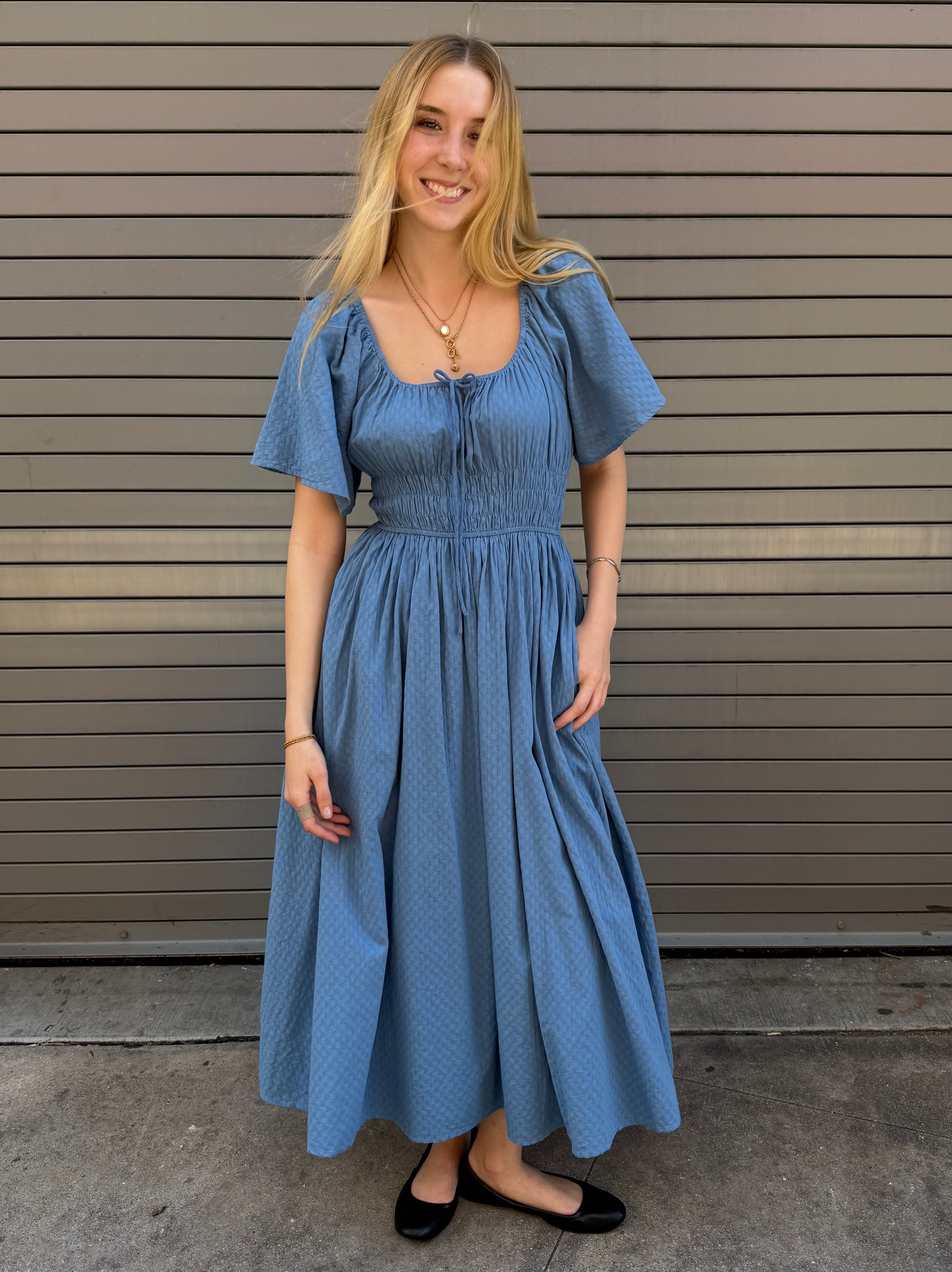 Woman wearing a blue dress standing in front of a metallic wall.