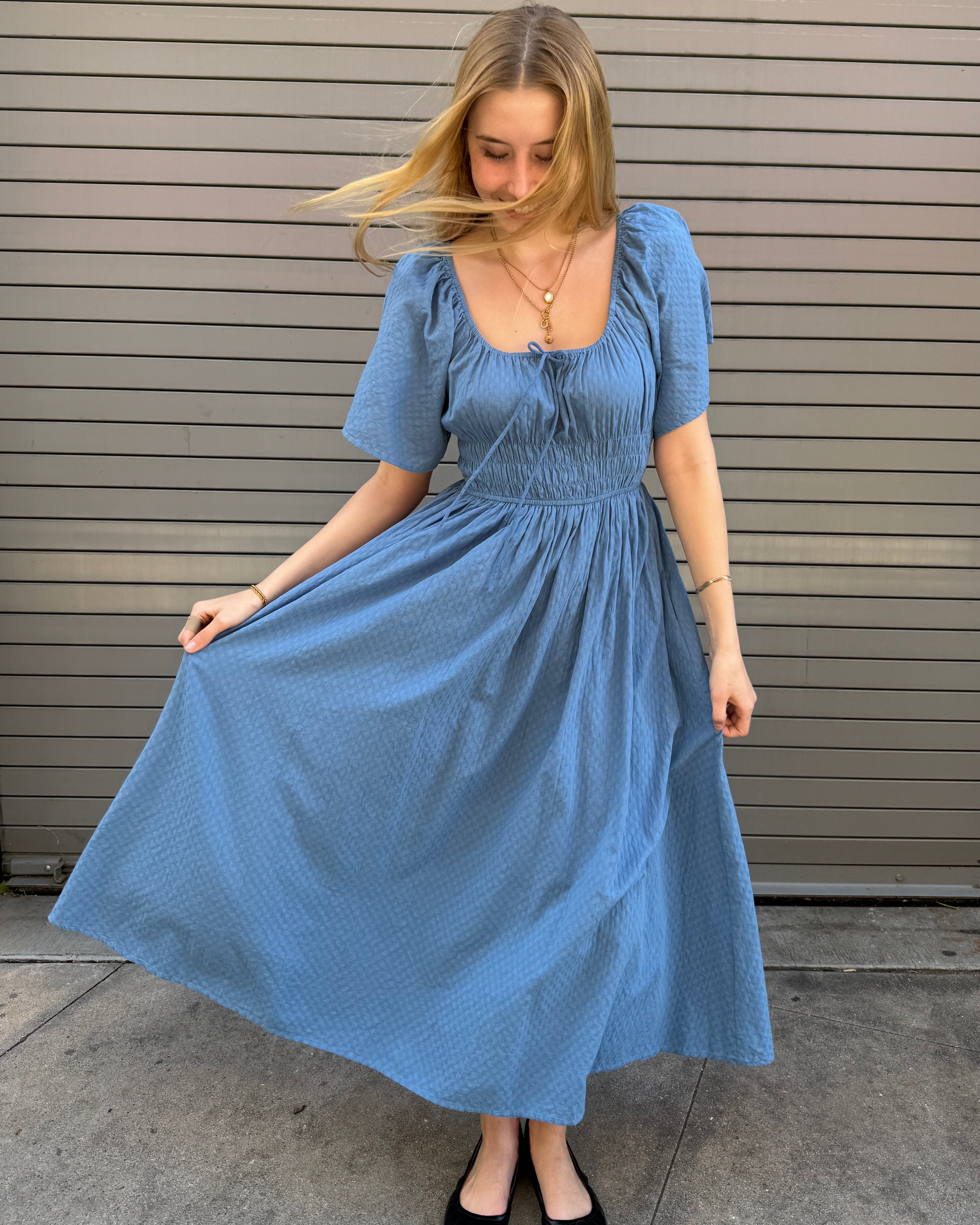 Woman wearing a blue dress standing on a concrete floor.