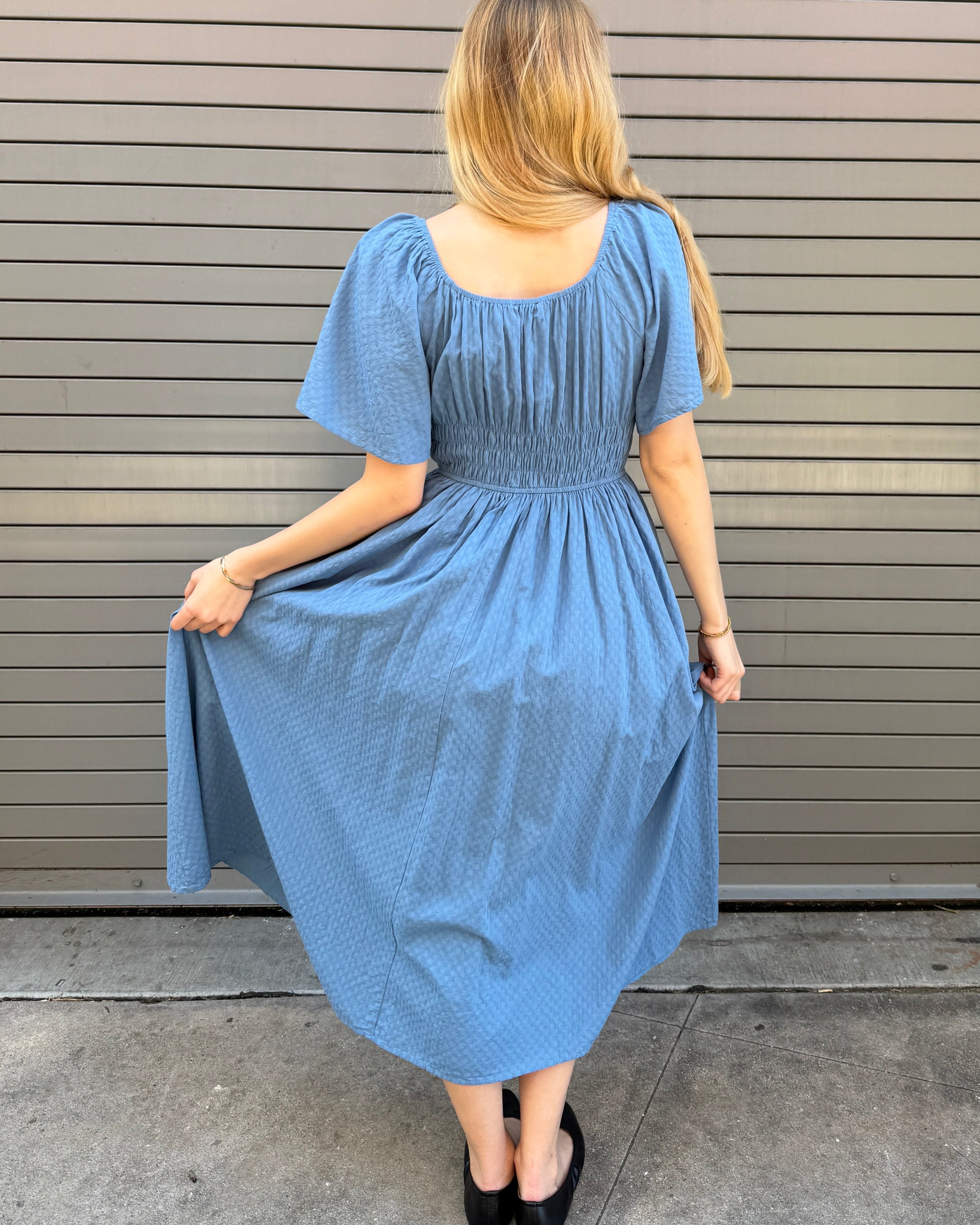 Woman wearing a blue dress standing against a metallic garage door.