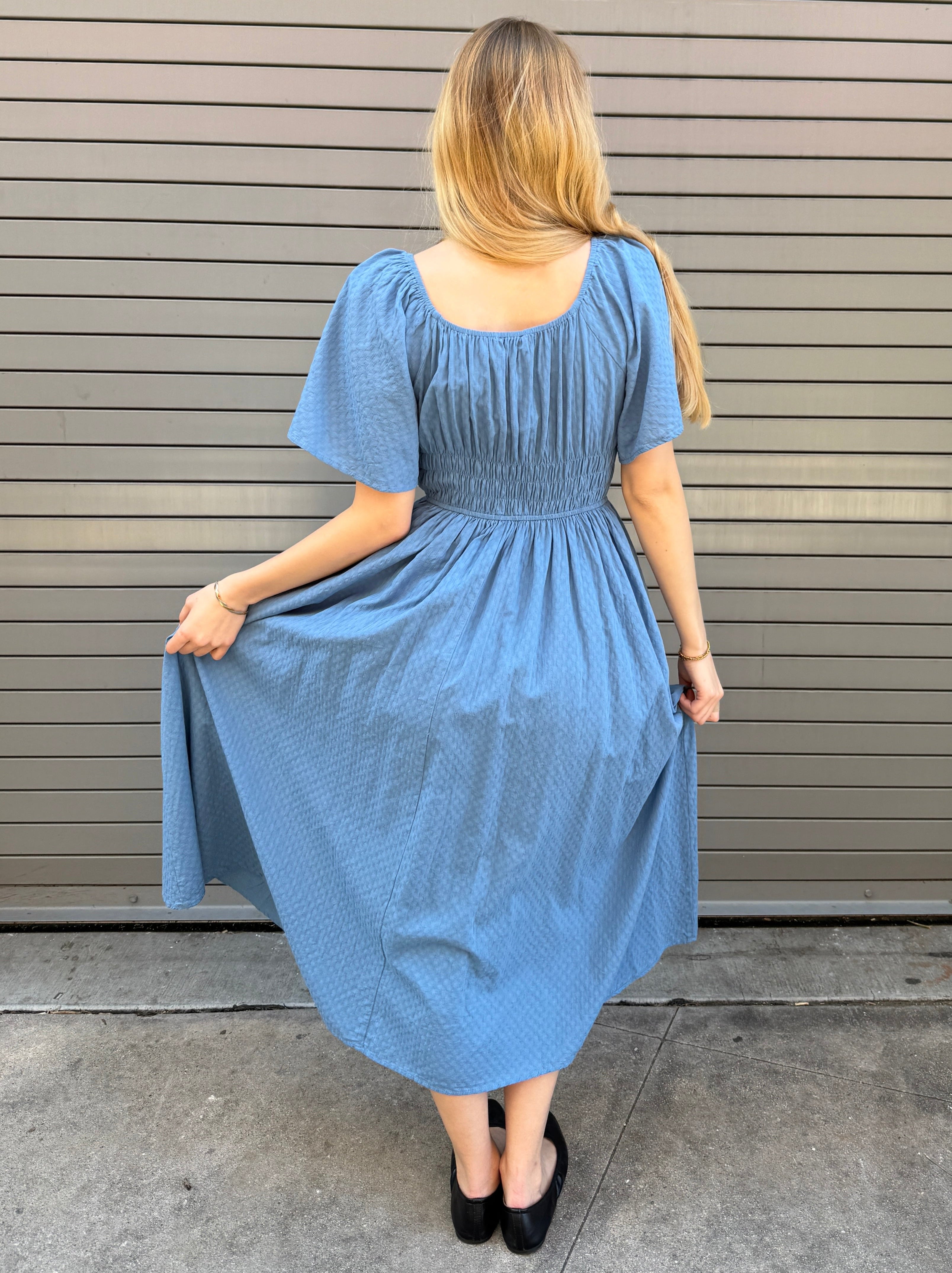 Woman wearing a blue dress standing against a metallic garage door.