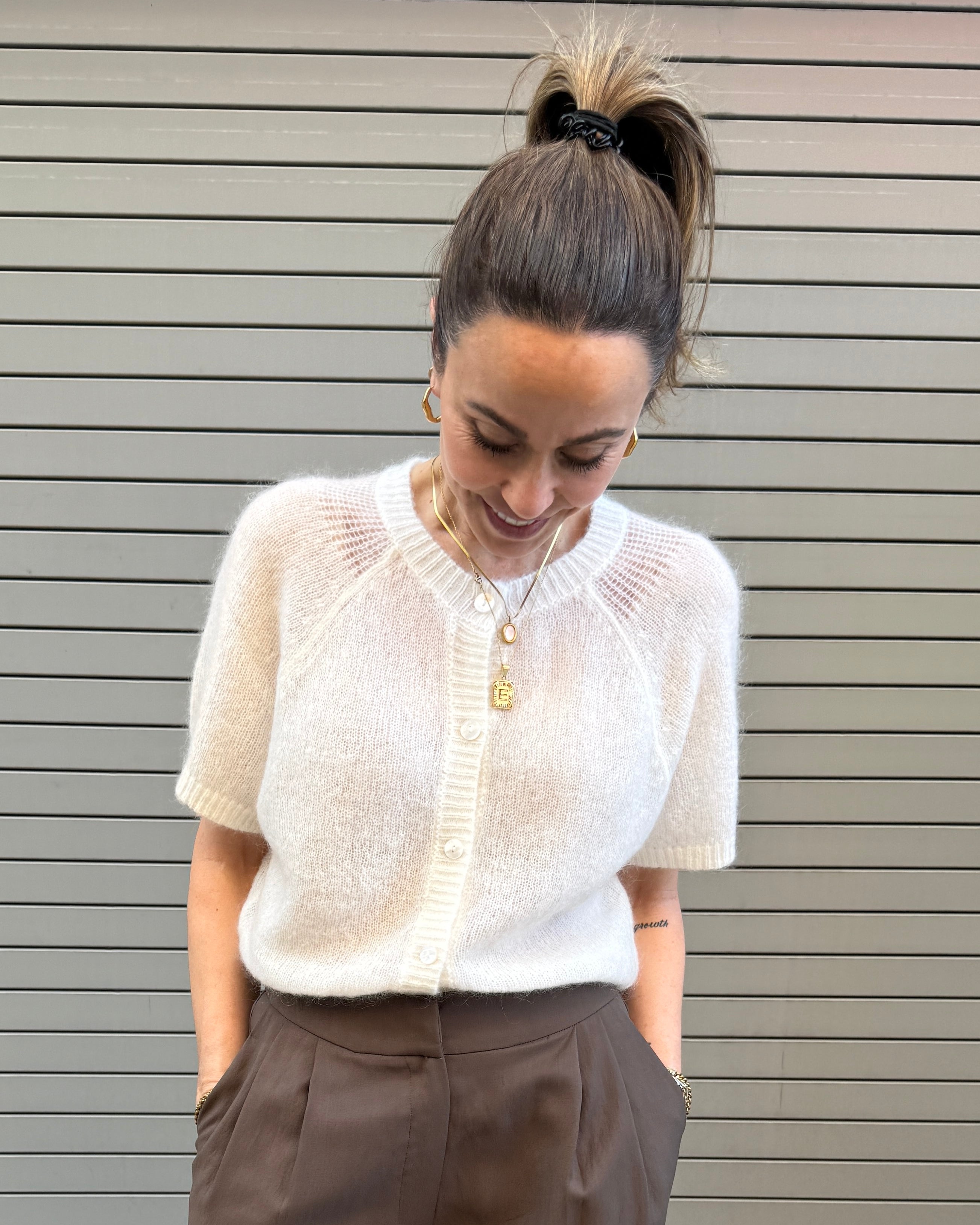 Woman wearing a white blouse and brown pants against a gray wall