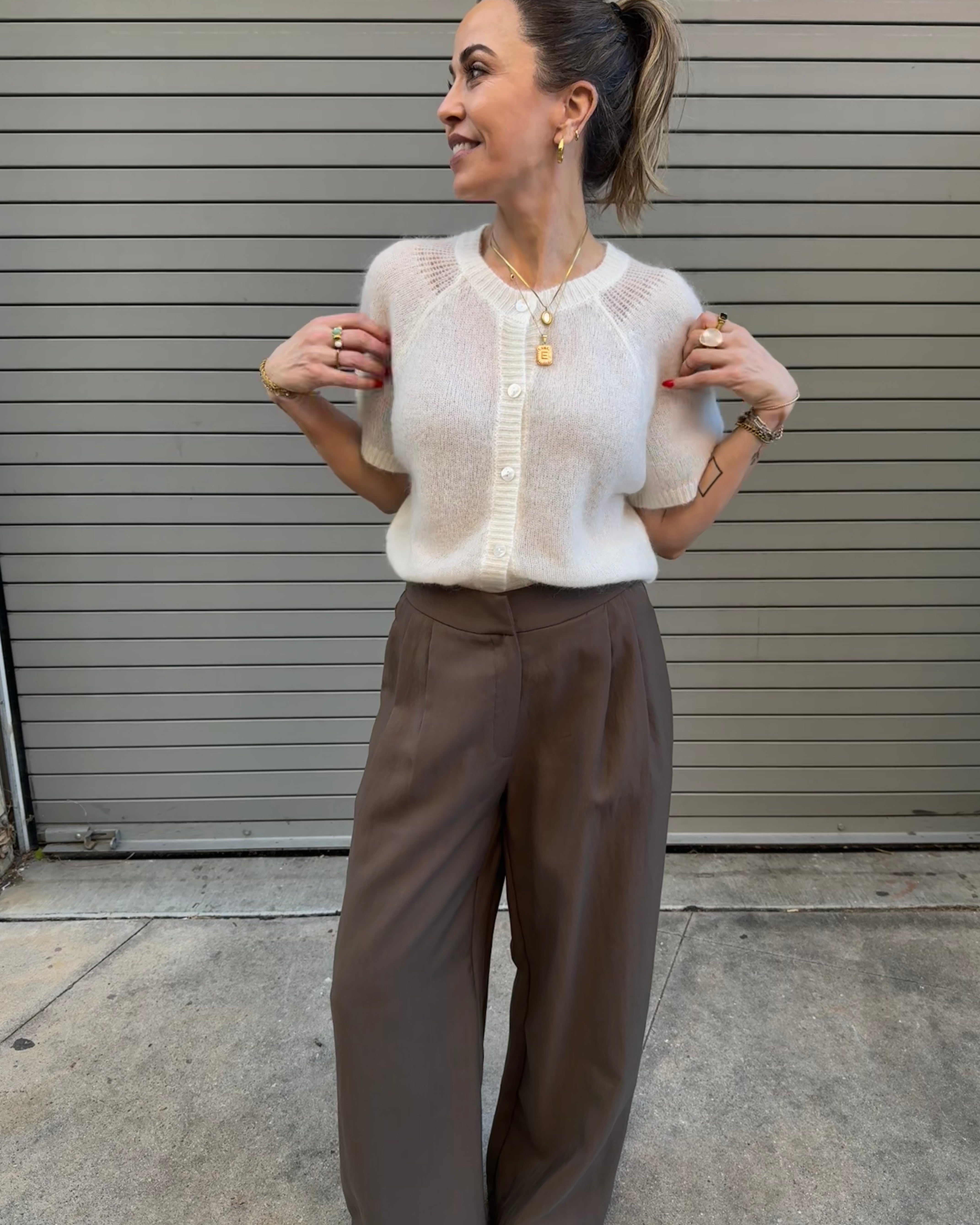Woman wearing a white blouse and brown pants standing against a metallic shutter.