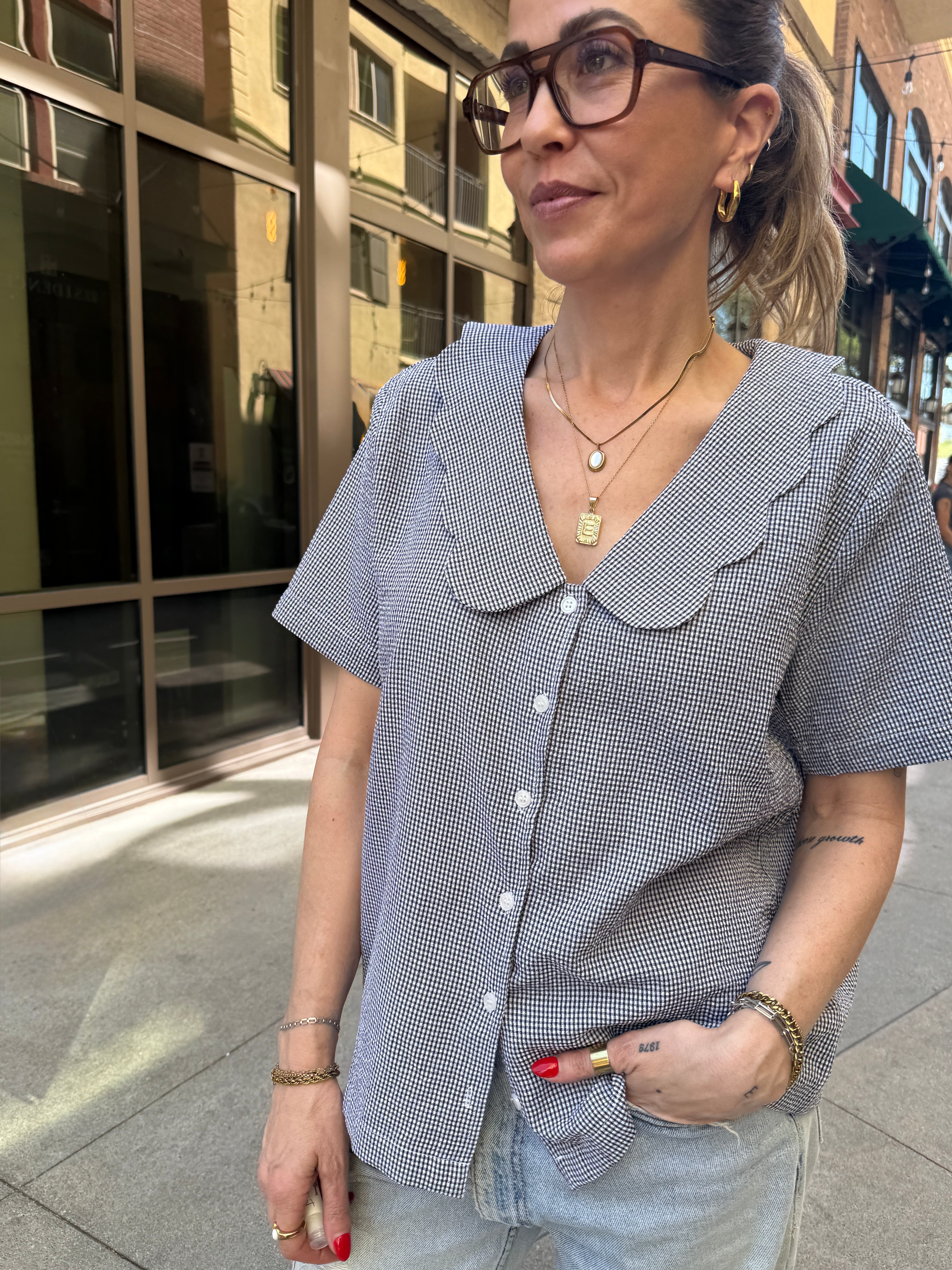 Woman wearing a patterned shirt and glasses outdoors.