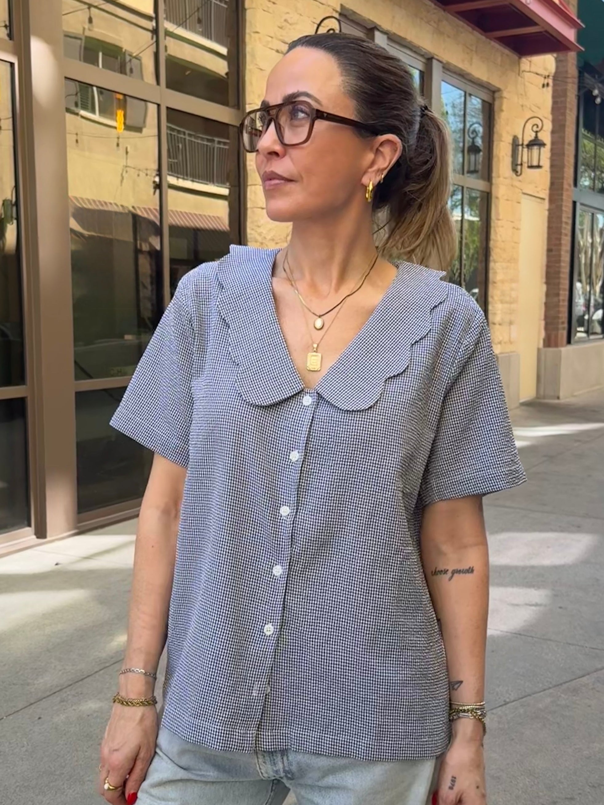 Woman wearing a short-sleeve button-up shirt with a large collar on a city street.