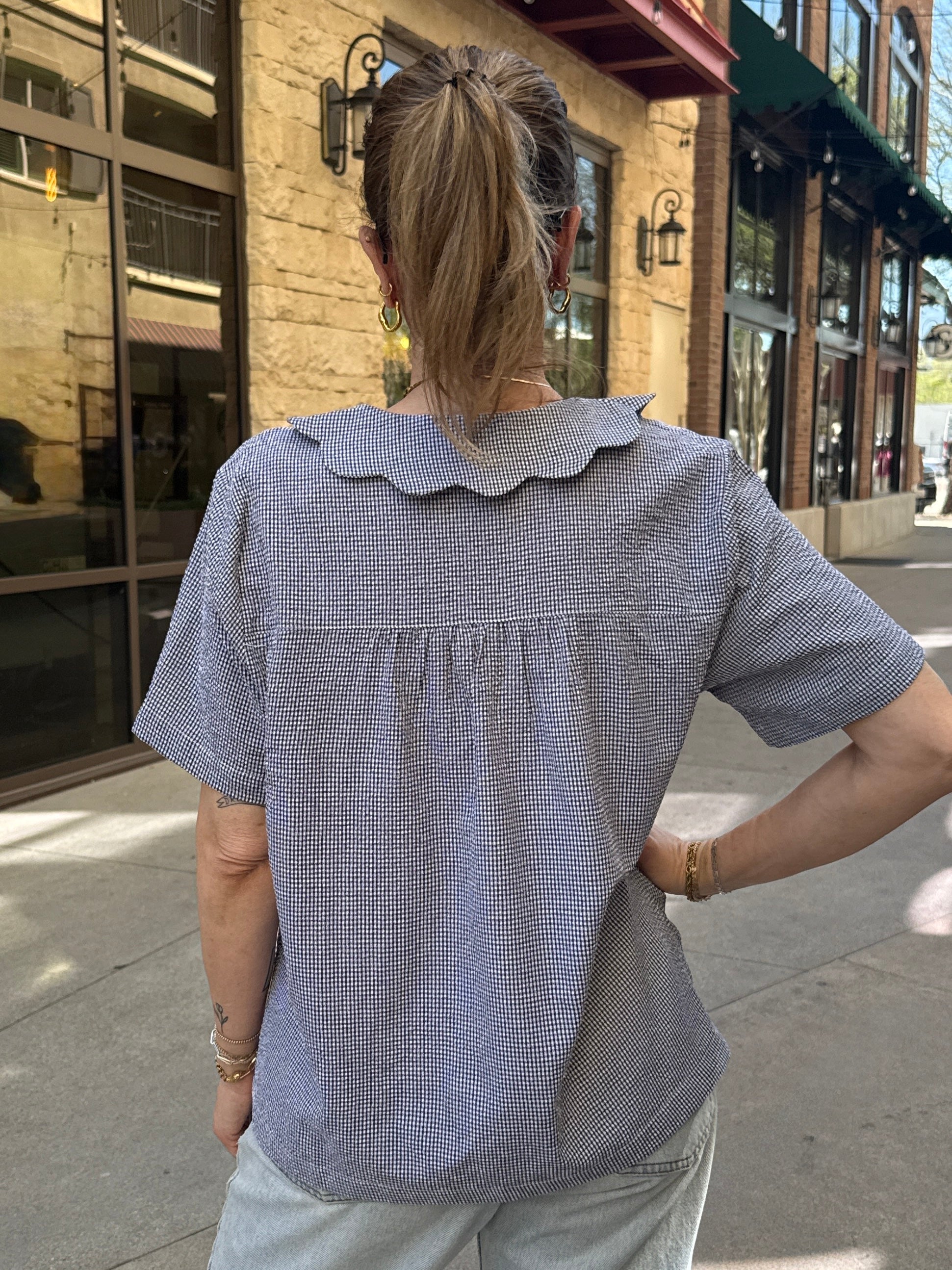 Person wearing a blue checkered shirt with a scalloped collar on a city street.