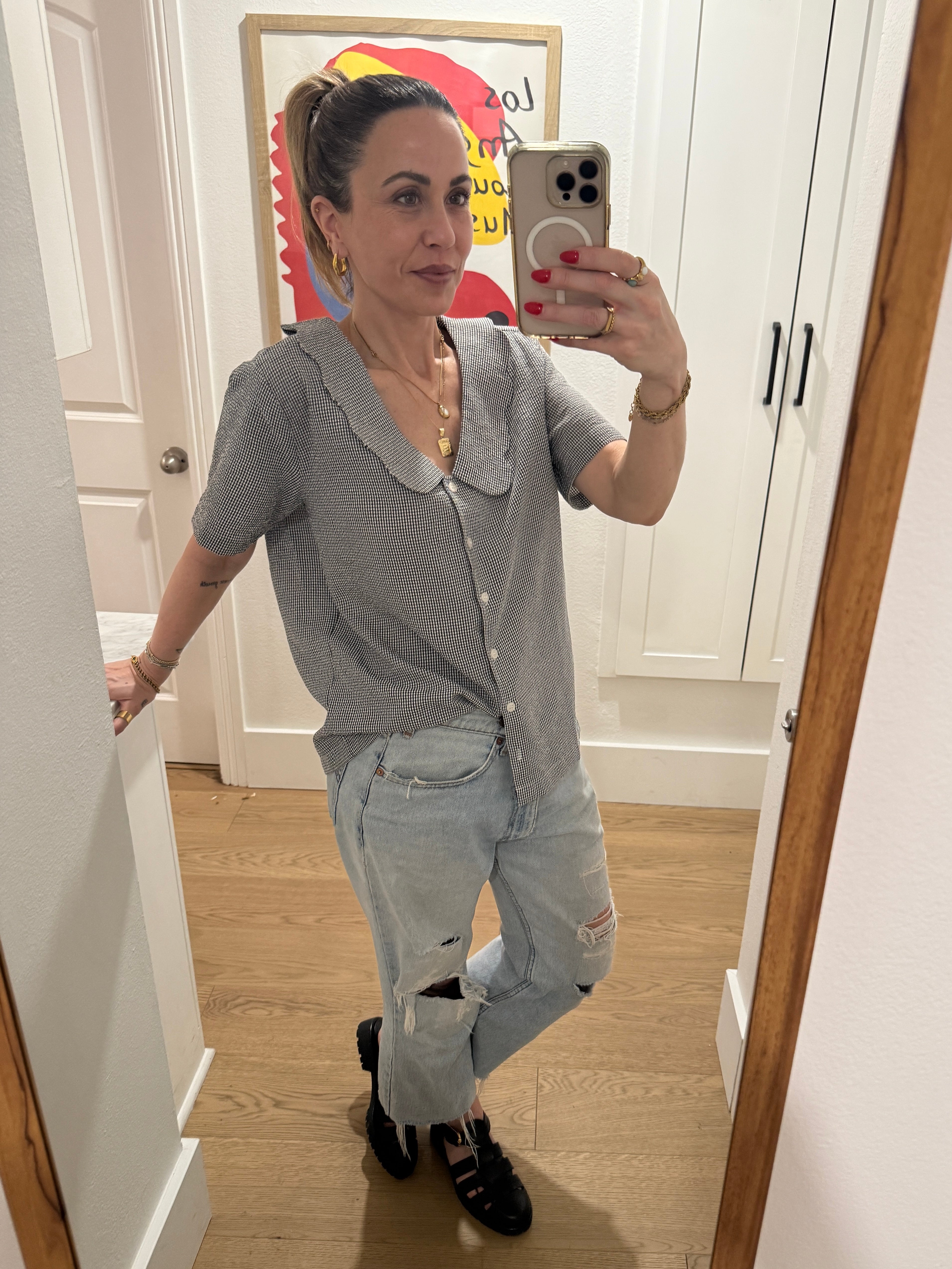 Woman taking a mirror selfie wearing a gray cardigan and jeans in a room with white walls and wooden floor.