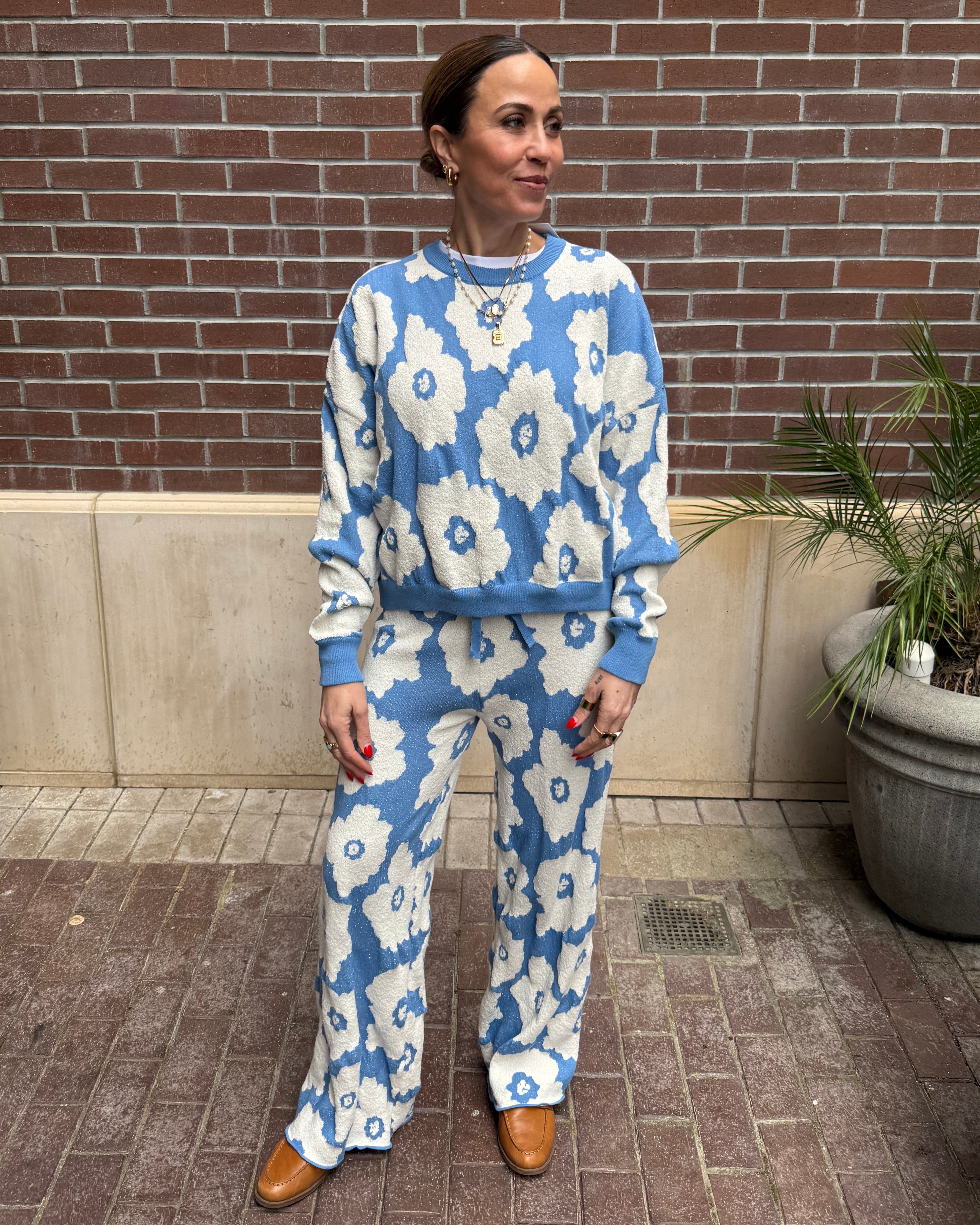 Woman wearing a blue and white floral outfit standing against a brick wall.