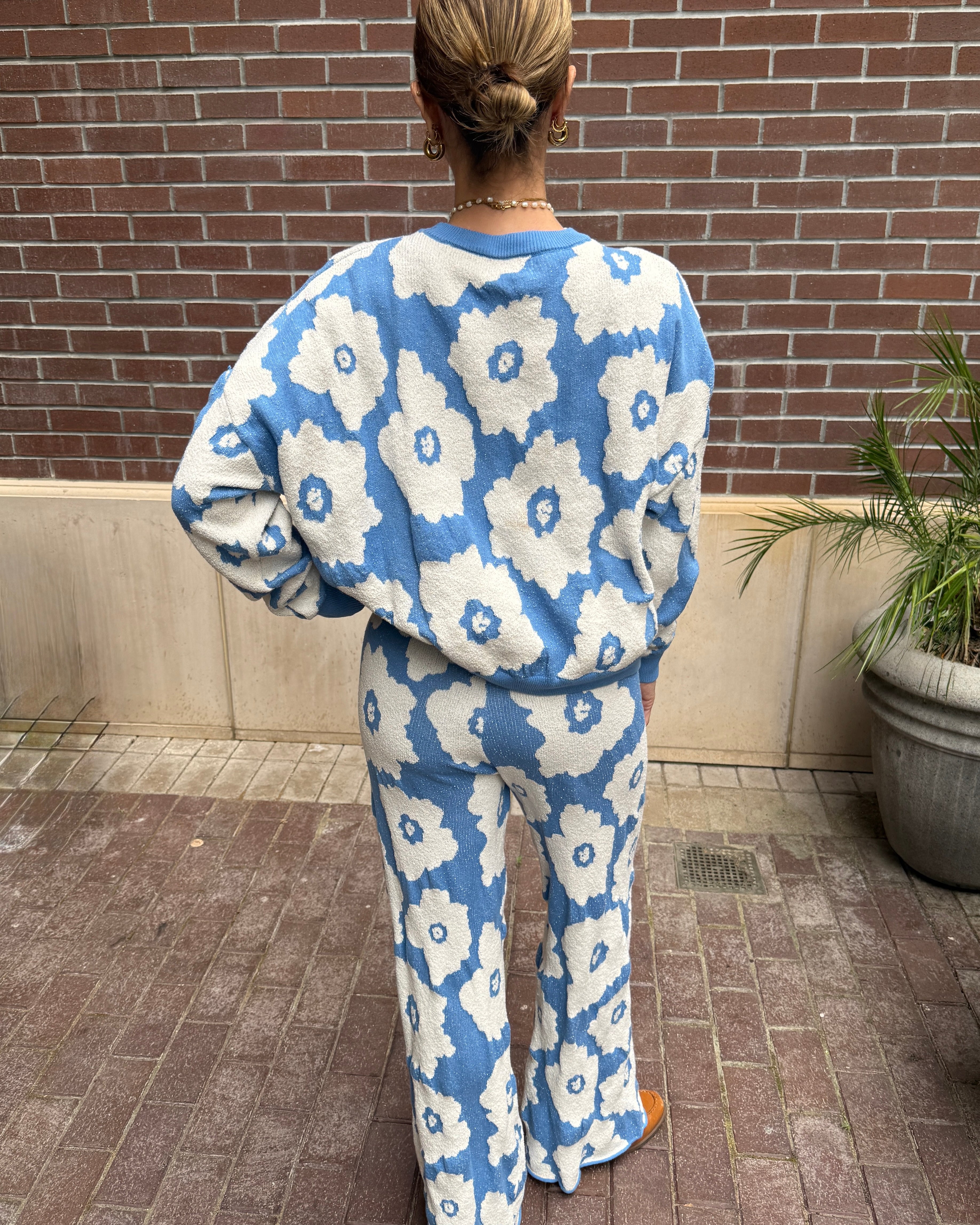 Person wearing a blue and white floral patterned outfit standing against a brick wall.