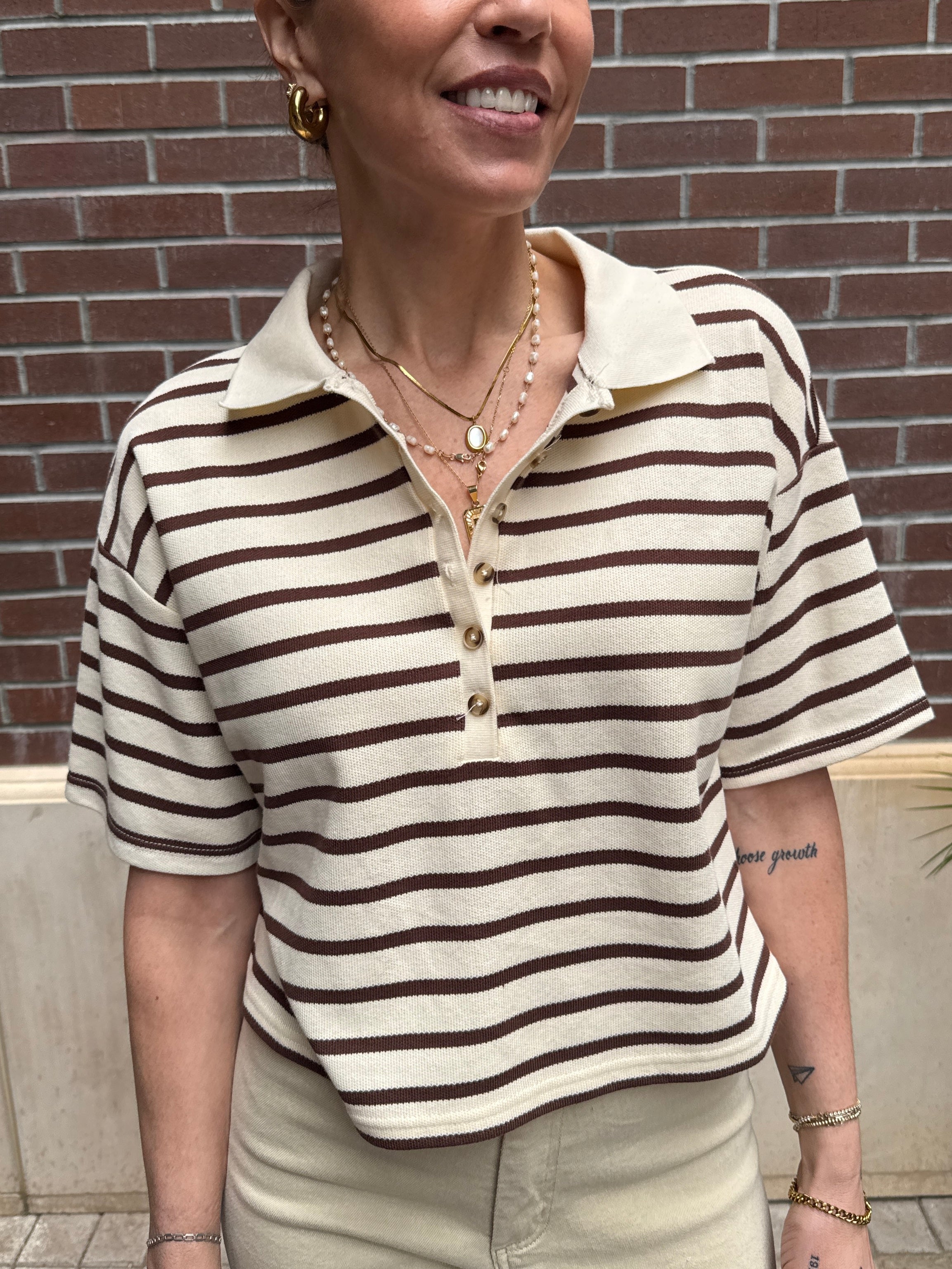 Person wearing a striped shirt standing against a brick wall.