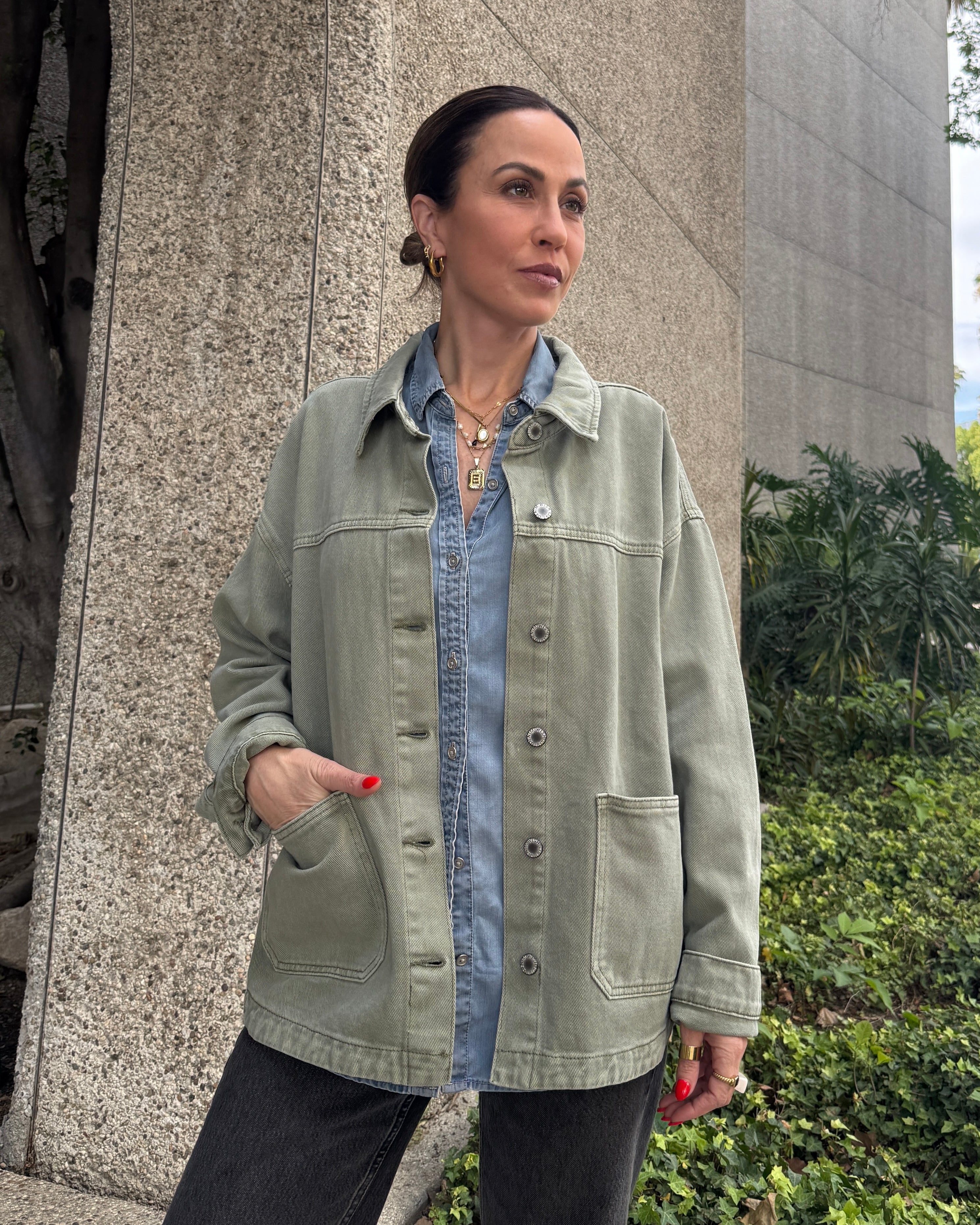 Woman wearing a green jacket over a denim shirt standing outdoors.