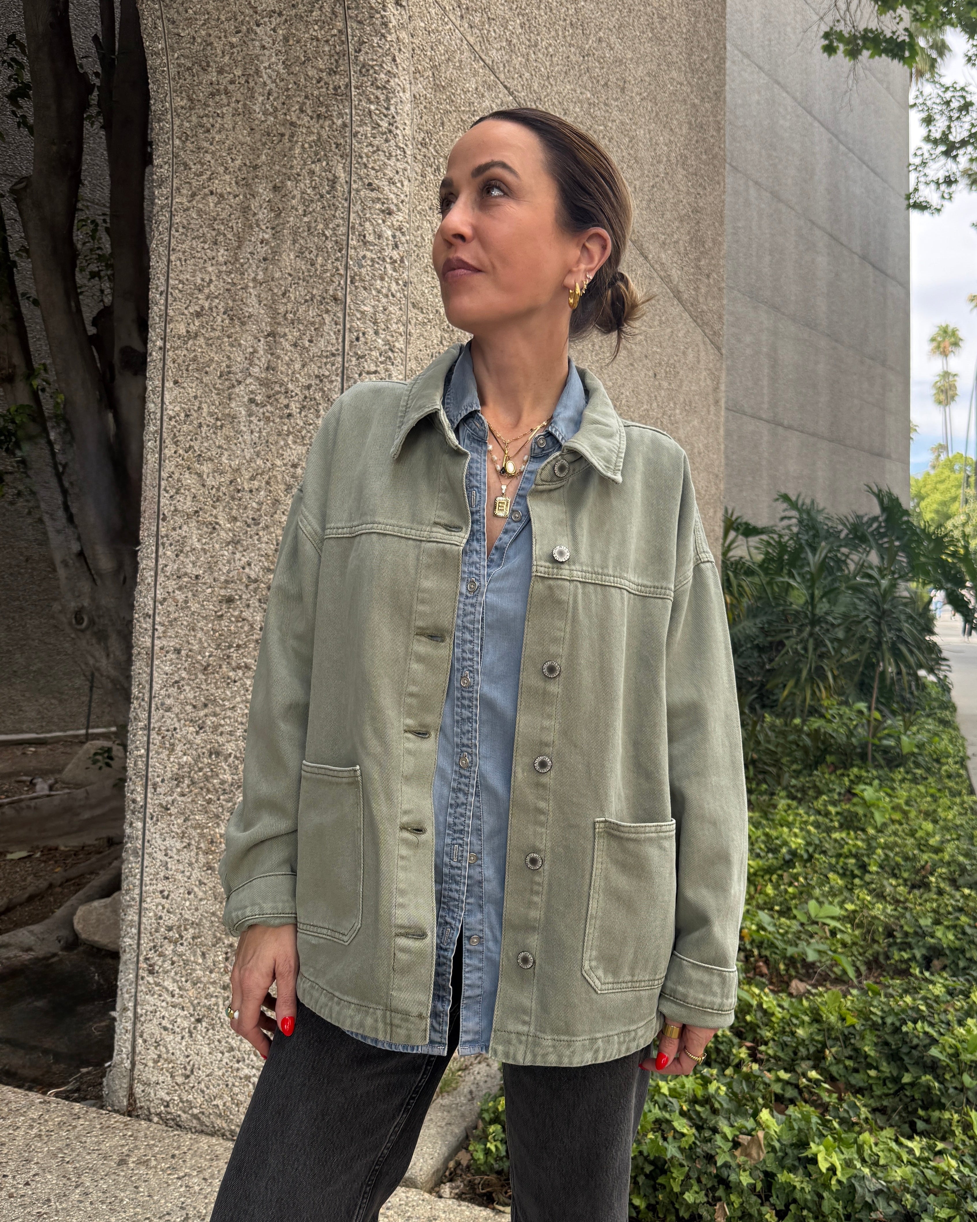 Woman standing on a sidewalk wearing a light green jacket over a denim shirt.